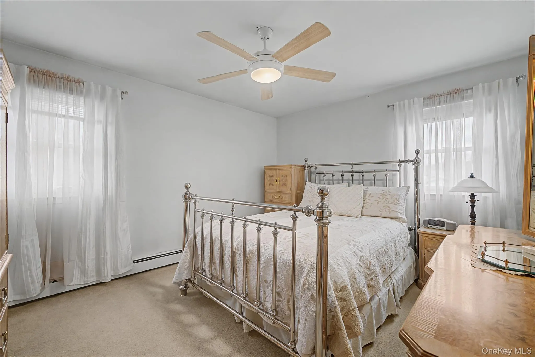 Bedroom featuring light carpet, a baseboard heating unit, and a ceiling fan Bedroom featuring light carpet, a baseboard heating unit, and a ceiling fan