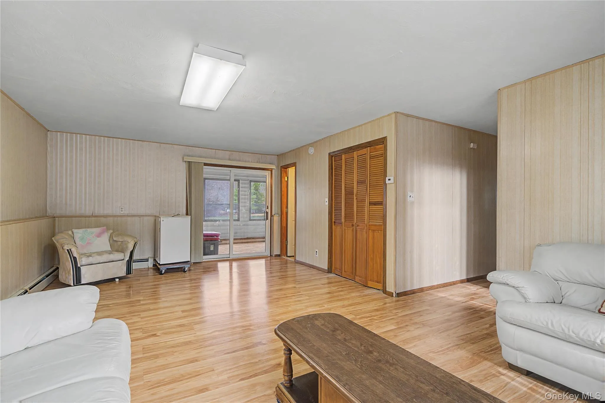 Living area featuring light wood-style floors, a baseboard radiator, and wallpapered walls Living area featuring light wood-style floors, a baseboard radiator, and wallpapered walls