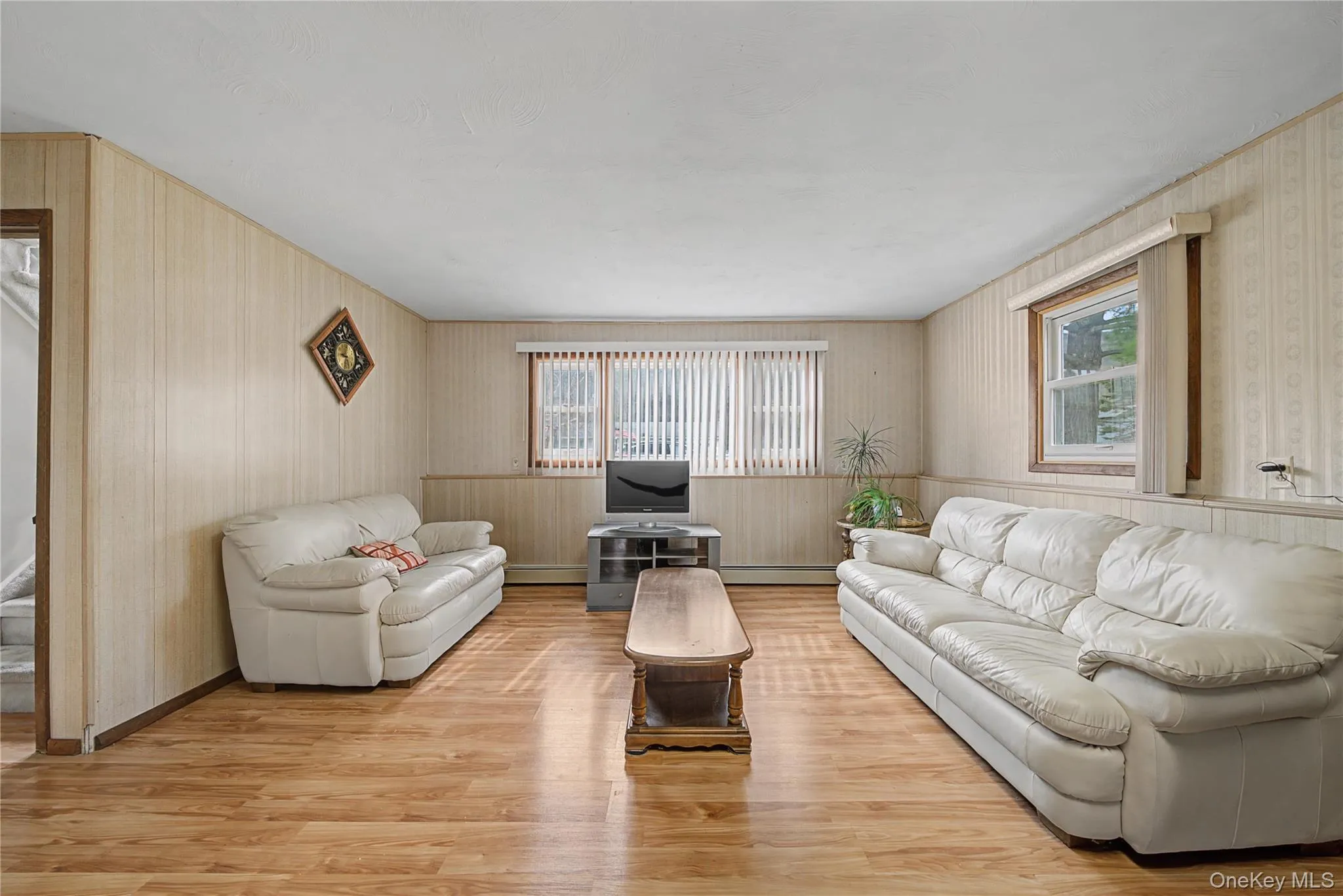 Living room with wood finished floors, wallpapered walls, healthy amount of natural light, and baseboard heating Living room with wood finished floors, wallpapered walls, healthy amount of natural light, and baseboard heating