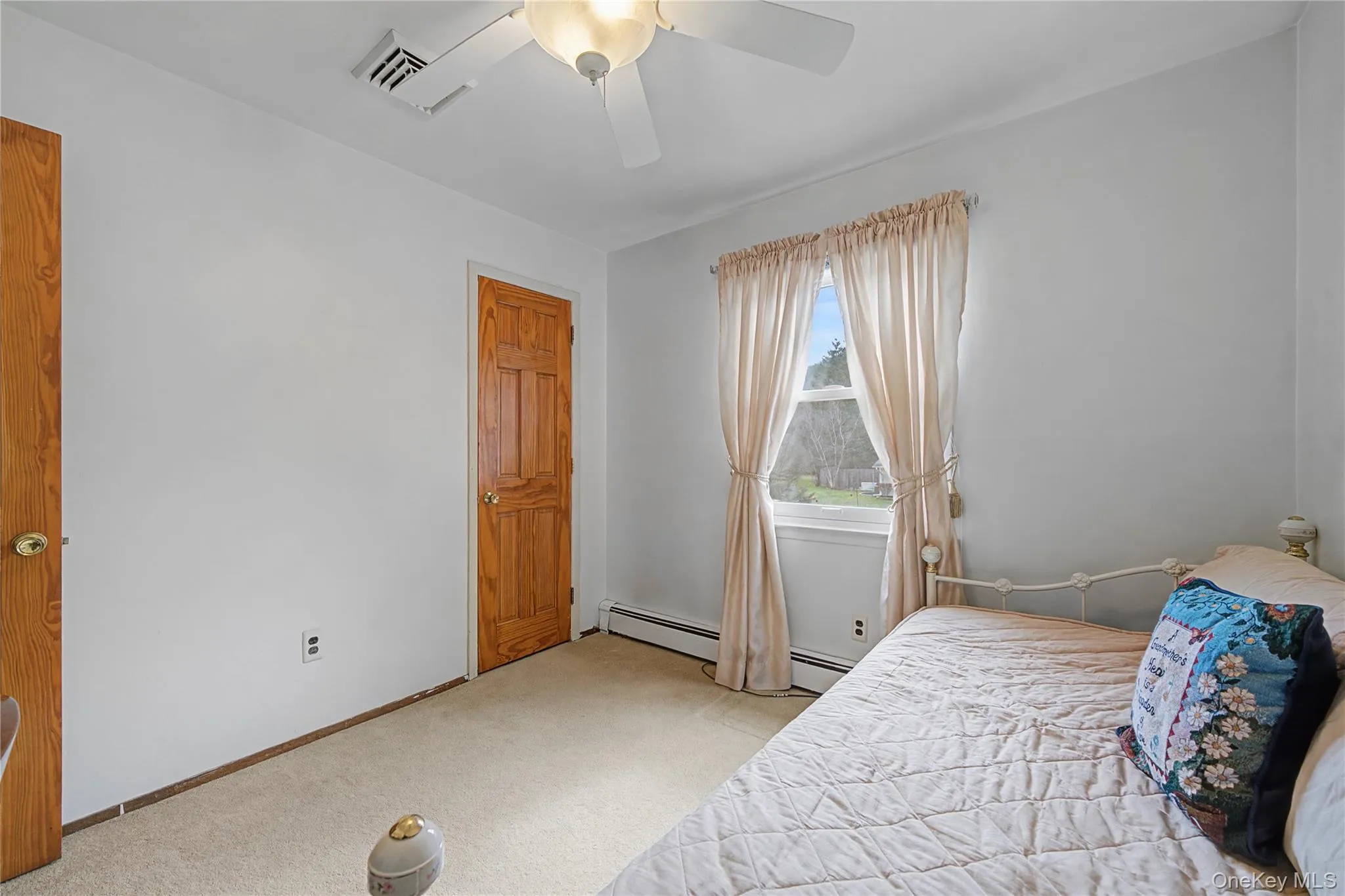 Bedroom featuring light carpet, ceiling fan, and a baseboard heating unit Bedroom featuring light carpet, ceiling fan, and a baseboard heating unit