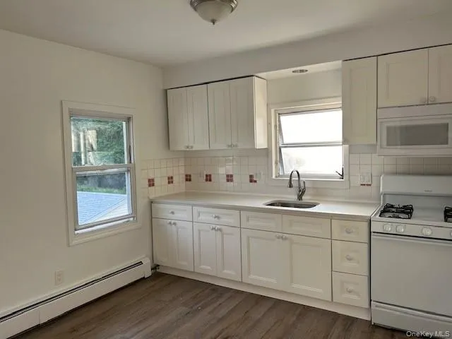 Kitchen featuring white cabinetry, white appliances, dark wood-type flooring, baseboard heating, and sink Kitchen featuring white cabinetry, white appliances, dark wood-type flooring, baseboard heating, and sink