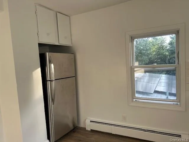 Kitchen with dark hardwood / wood-style flooring, stainless steel refrigerator, baseboard heating, and white cabinets Kitchen with dark hardwood / wood-style flooring, stainless steel refrigerator, baseboard heating, and white cabinets