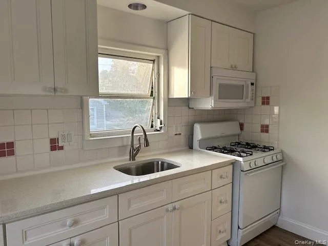 Kitchen featuring white cabinetry, tasteful backsplash, white appliances, sink, and dark hardwood / wood-style floors Kitchen featuring white cabinetry, tasteful backsplash, white appliances, sink, and dark hardwood / wood-style floors