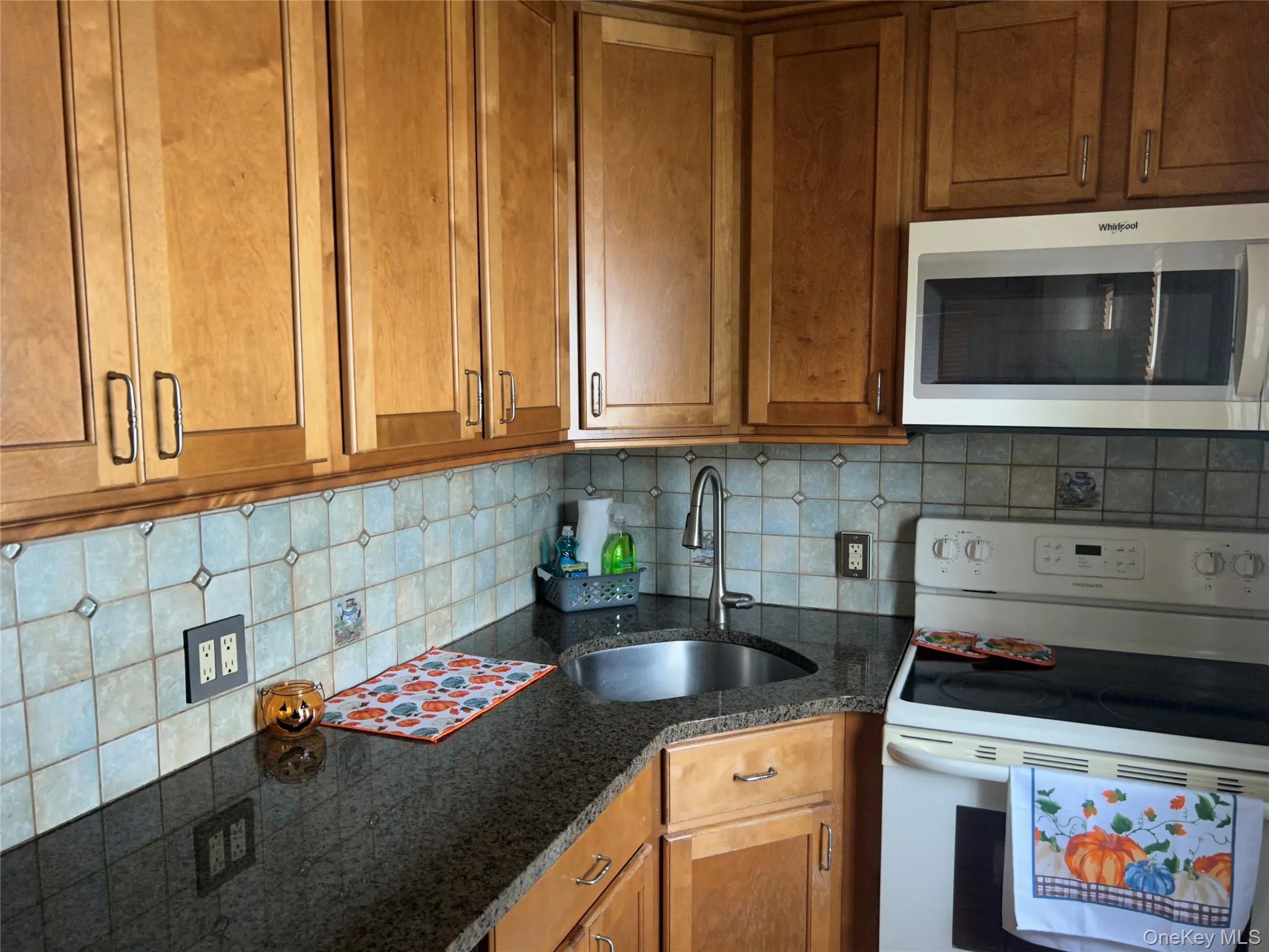 Kitchen featuring white electric range oven, decorative backsplash, dark stone counters, and brown cabinets Kitchen featuring white electric range oven, decorative backsplash, dark stone counters, and brown cabinets