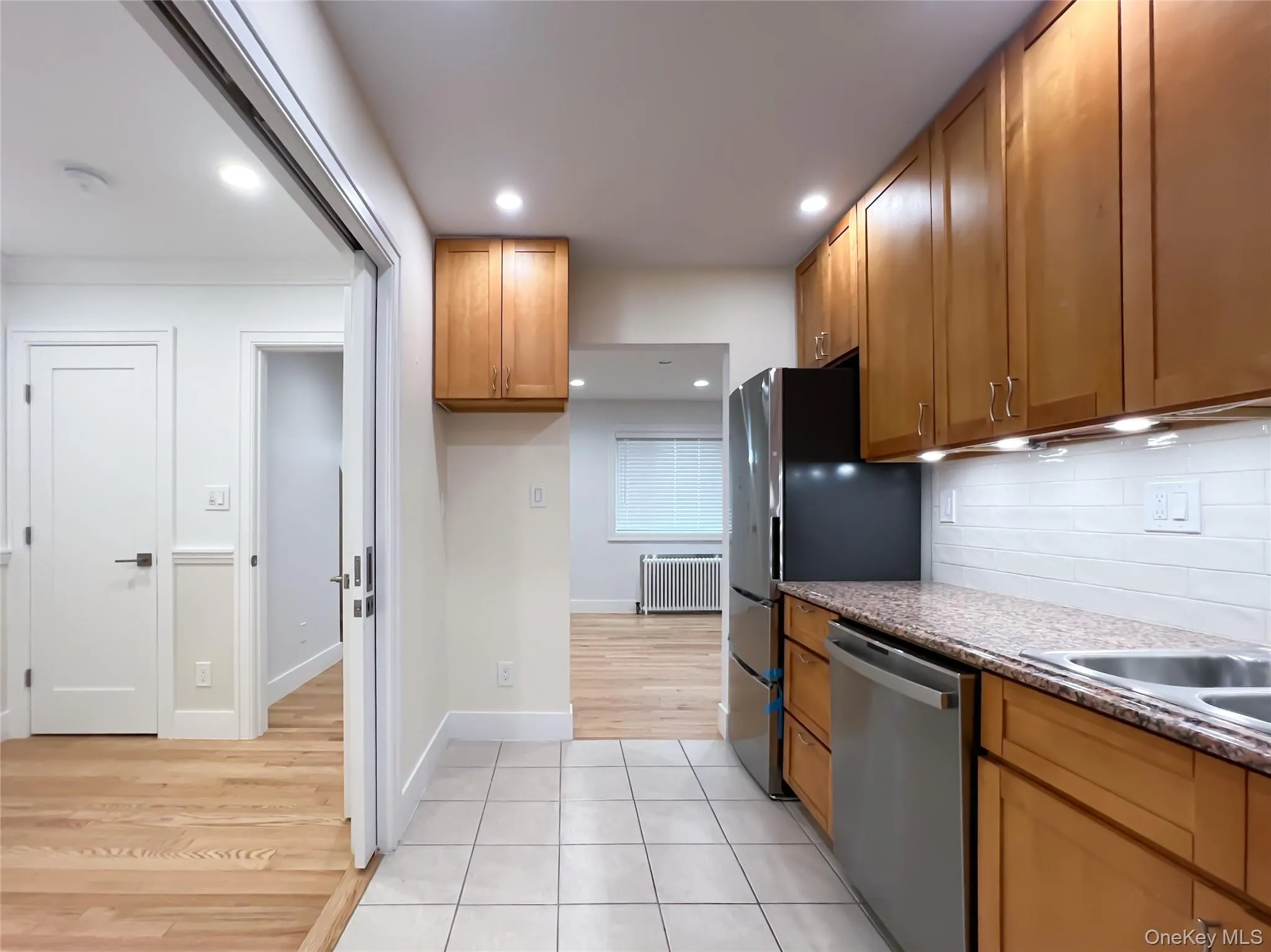 Kitchen featuring light tile patterned floors, stainless steel dishwasher, light stone counters, recessed lighting, and radiator Kitchen featuring light tile patterned floors, stainless steel dishwasher, light stone counters, recessed lighting, and radiator