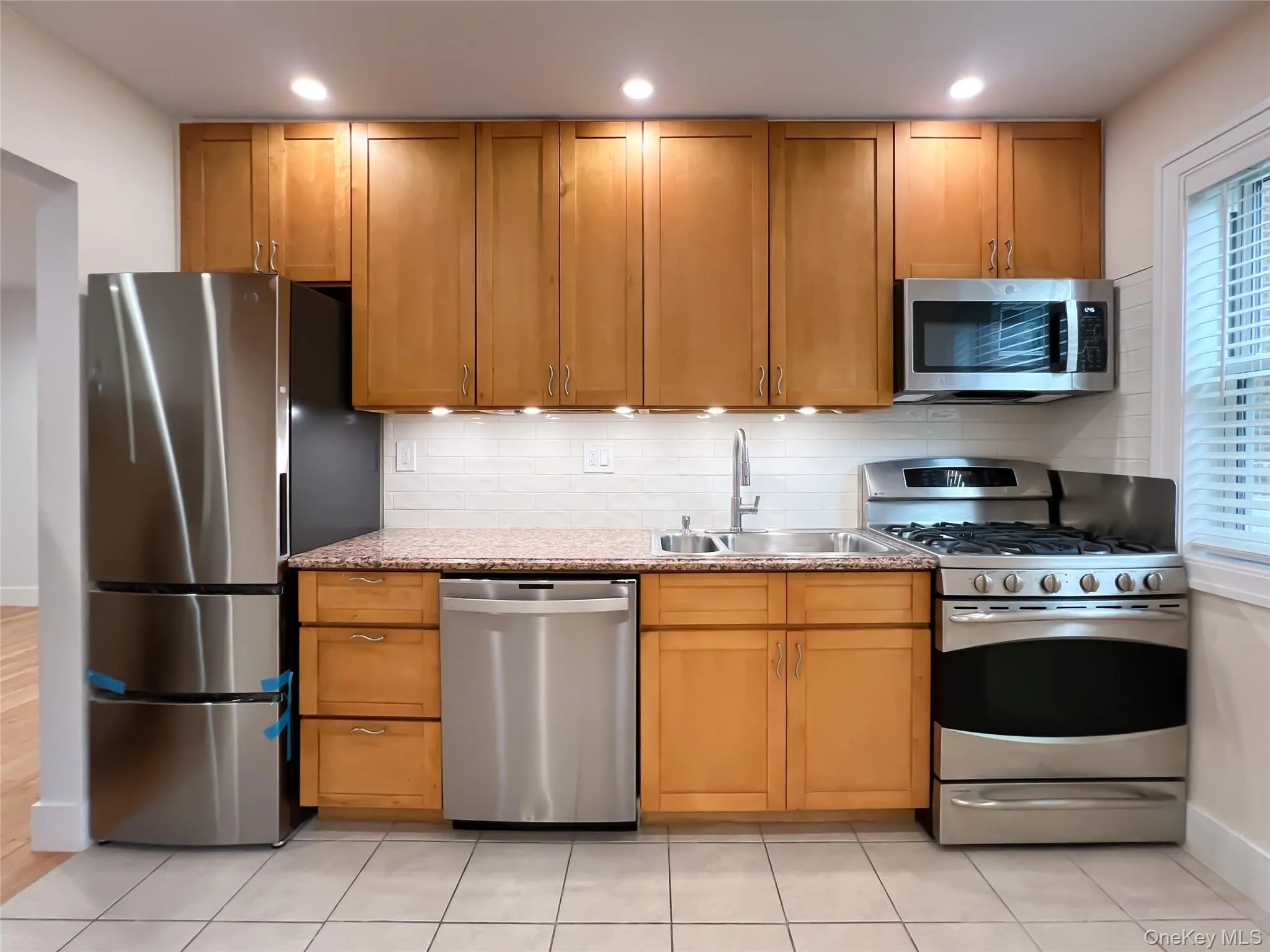 Kitchen with decorative backsplash, appliances with stainless steel finishes, light stone countertops, light tile patterned floors, and recessed lighting Kitchen with decorative backsplash, appliances with stainless steel finishes, light stone countertops, light tile patterned floors, and recessed lighting