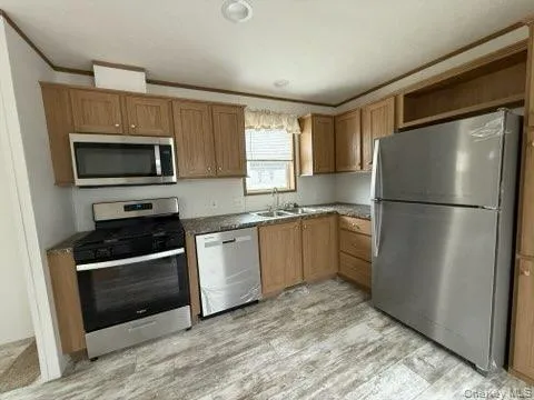 Kitchen with brown cabinetry, ornamental molding, a sink, light wood-style flooring, and stainless steel appliances Kitchen with brown cabinetry, ornamental molding, a sink, light wood-style flooring, and stainless steel appliances