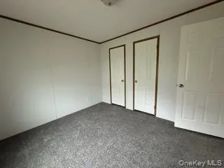 Unfurnished bedroom featuring dark colored carpet and multiple closets Unfurnished bedroom featuring dark colored carpet and multiple closets
