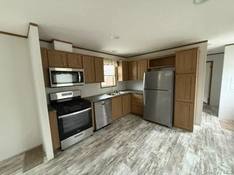 Kitchen with ornamental molding, light wood-type flooring, brown cabinets, a sink, and appliances with stainless steel finishes Kitchen with ornamental molding, light wood-type flooring, brown cabinets, a sink, and appliances with stainless steel finishes