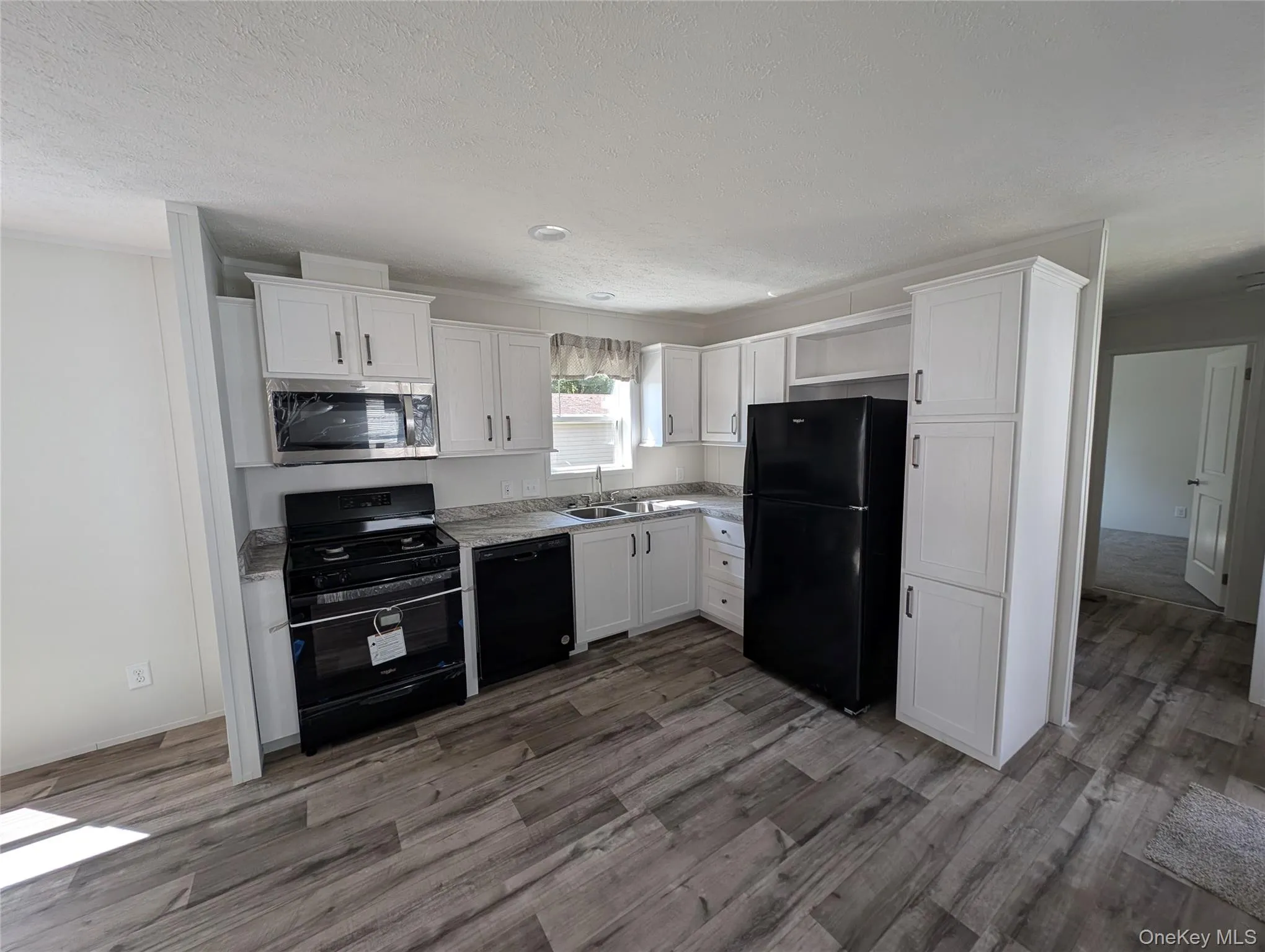 Kitchen featuring a sink, white cabinetry, wood finished floors, and black appliances Kitchen featuring a sink, white cabinetry, wood finished floors, and black appliances