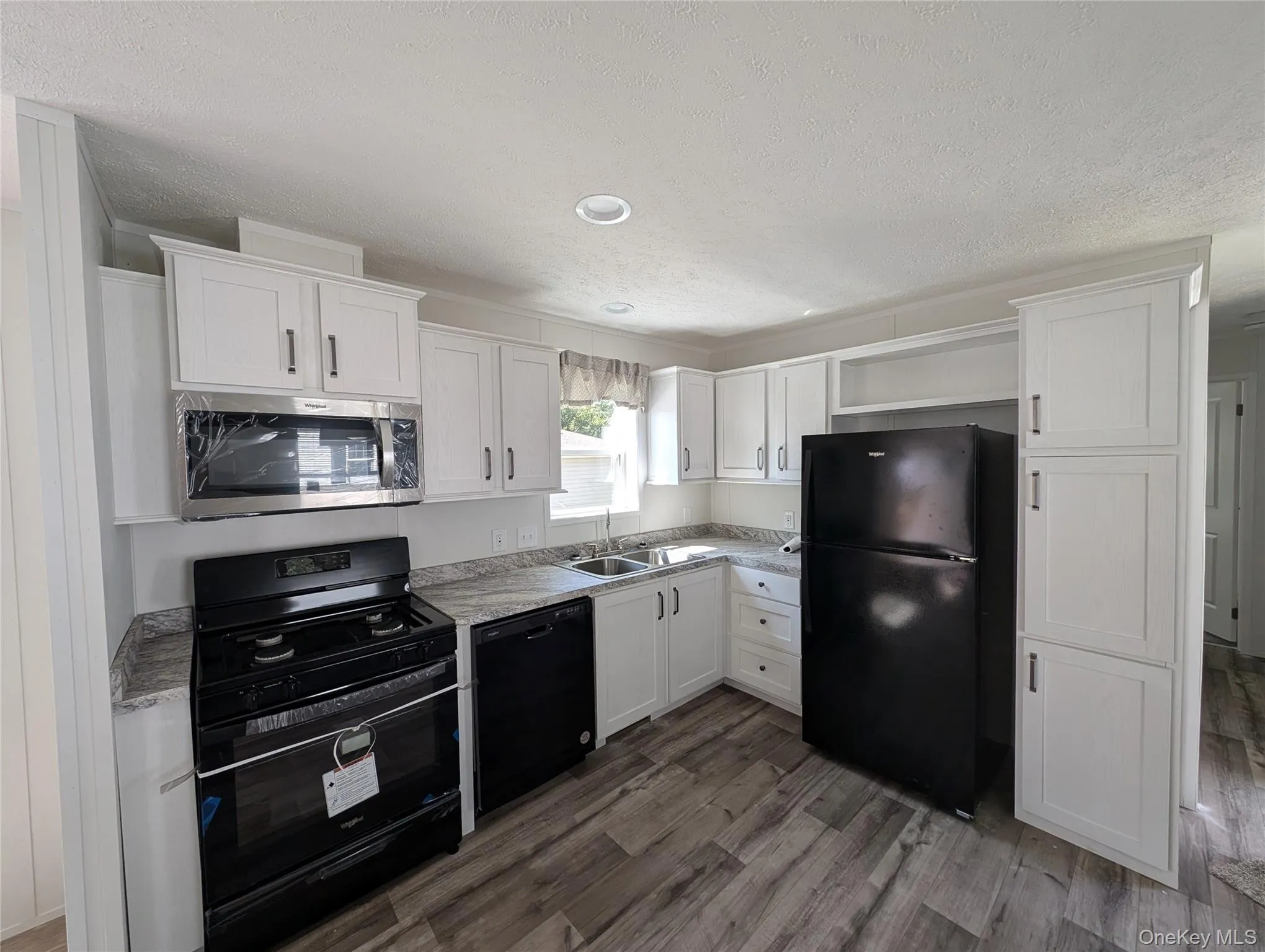 Kitchen with a sink, black appliances, a textured ceiling, and white cabinetry Kitchen with a sink, black appliances, a textured ceiling, and white cabinetry