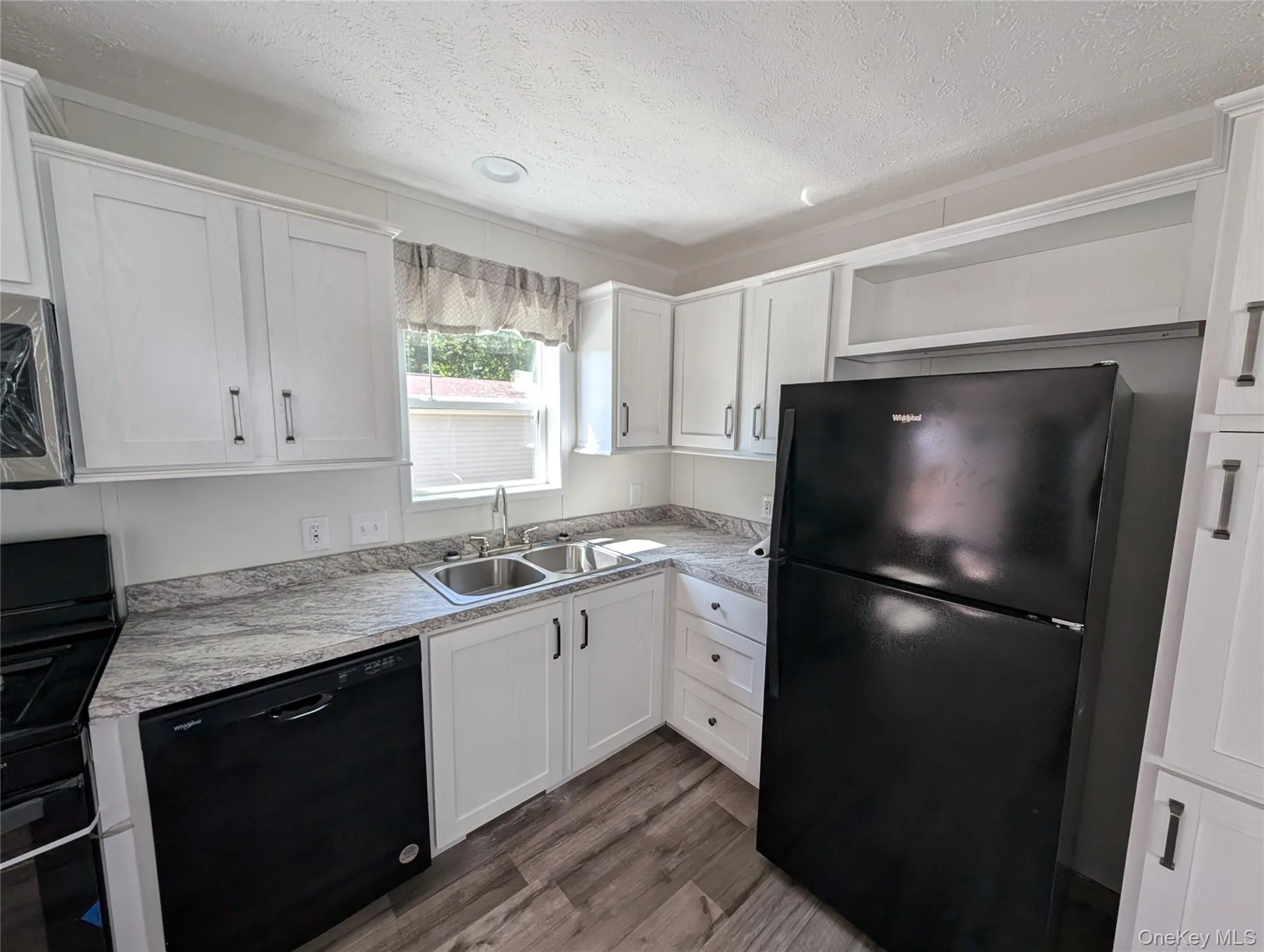 Kitchen featuring dark wood-style flooring, a textured ceiling, a sink, light countertops, and black appliances Kitchen featuring dark wood-style flooring, a textured ceiling, a sink, light countertops, and black appliances