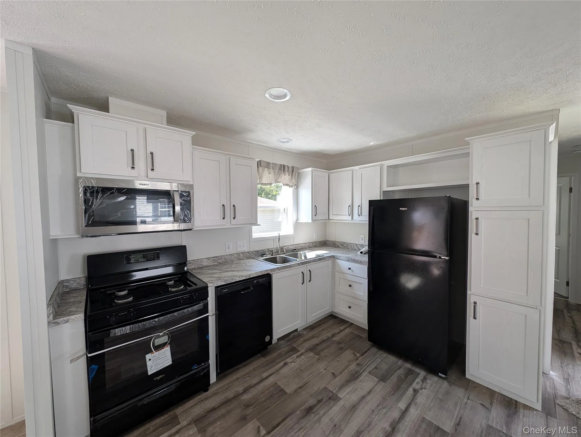 Kitchen featuring white cabinetry, a textured ceiling, a sink, and black appliances Kitchen featuring white cabinetry, a textured ceiling, a sink, and black appliances
