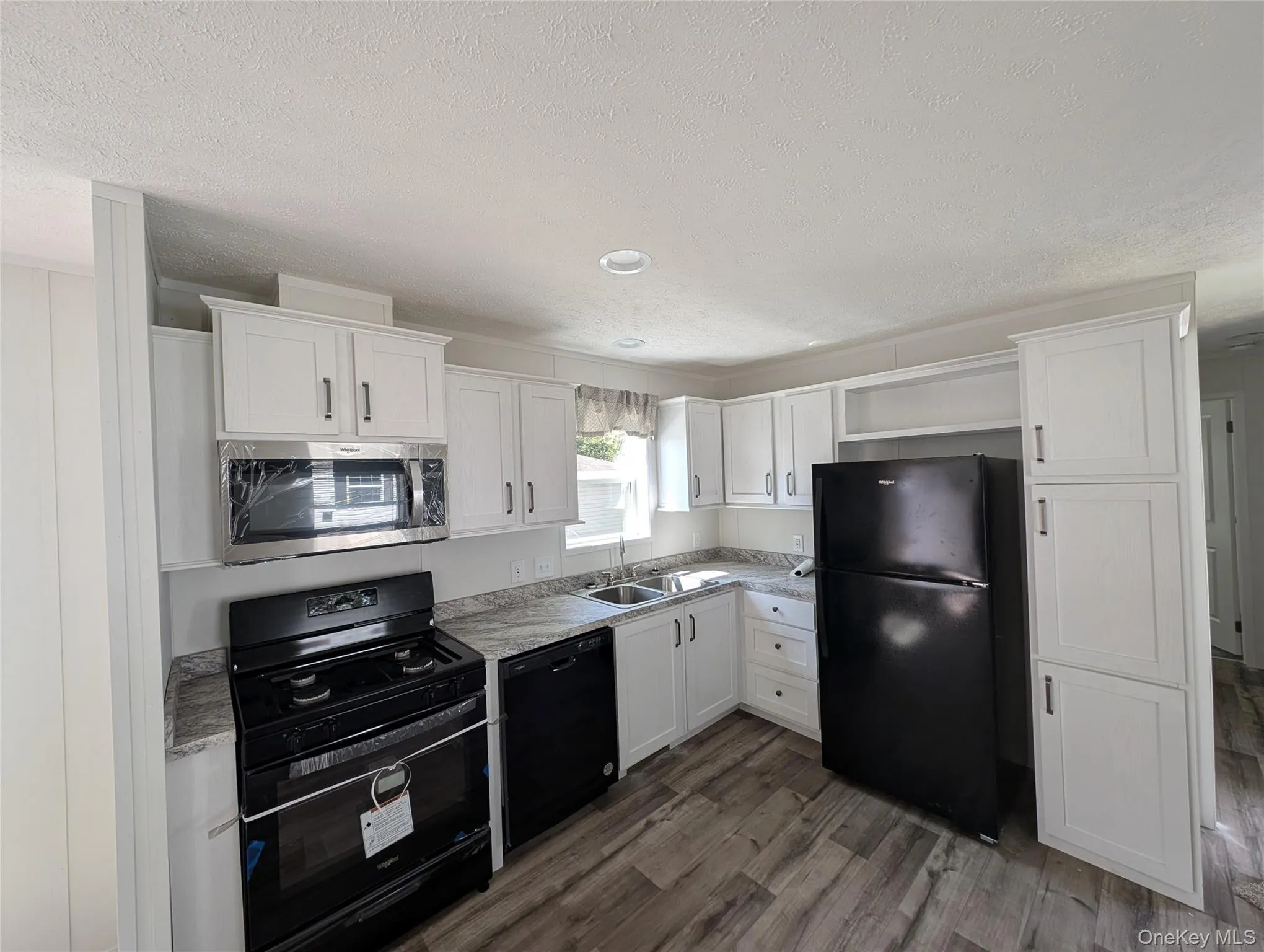 Kitchen with a textured ceiling, wood finished floors, a sink, white cabinets, and black appliances Kitchen with a textured ceiling, wood finished floors, a sink, white cabinets, and black appliances