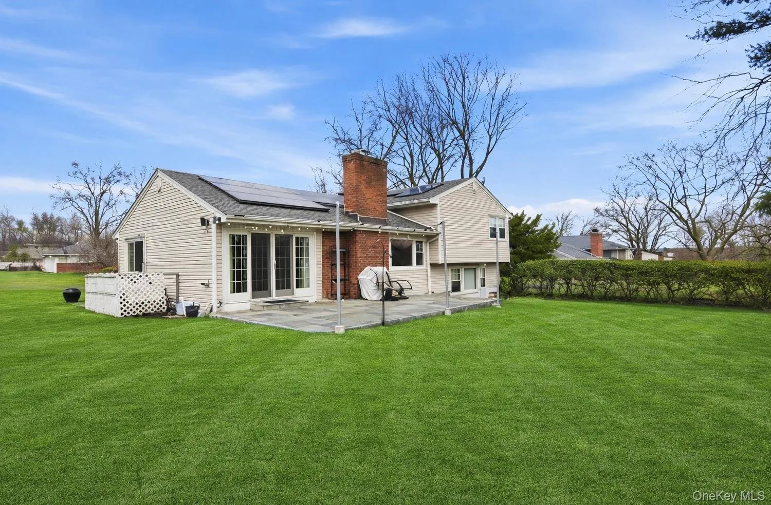 Back of house with solar panels, a yard, a chimney, and a patio Back of house with solar panels, a yard, a chimney, and a patio