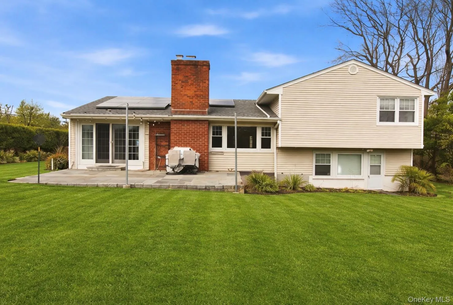 Back of house with solar panels, a chimney, a yard, a patio area, and roof with shingles Back of house with solar panels, a chimney, a yard, a patio area, and roof with shingles