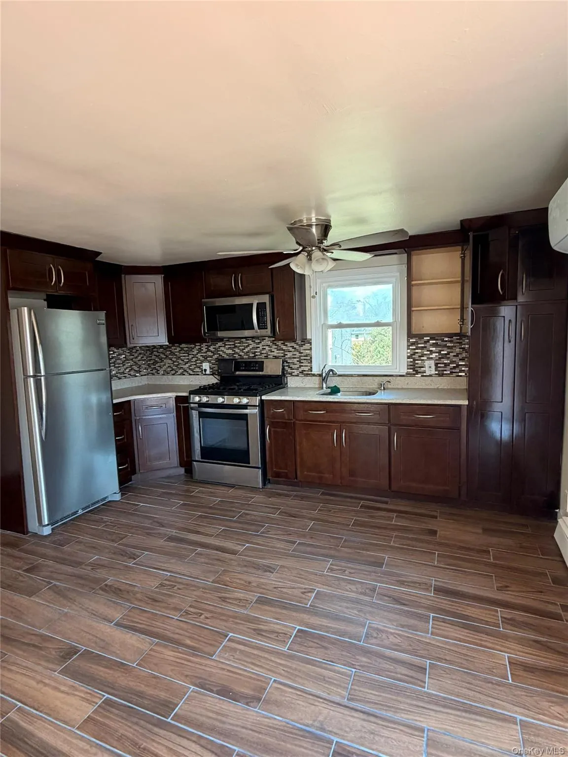 Kitchen featuring stainless steel appliances, light countertops, wood finish floors, and dark wood finish cabinetry Kitchen featuring stainless steel appliances, light countertops, wood finish floors, and dark wood finish cabinetry