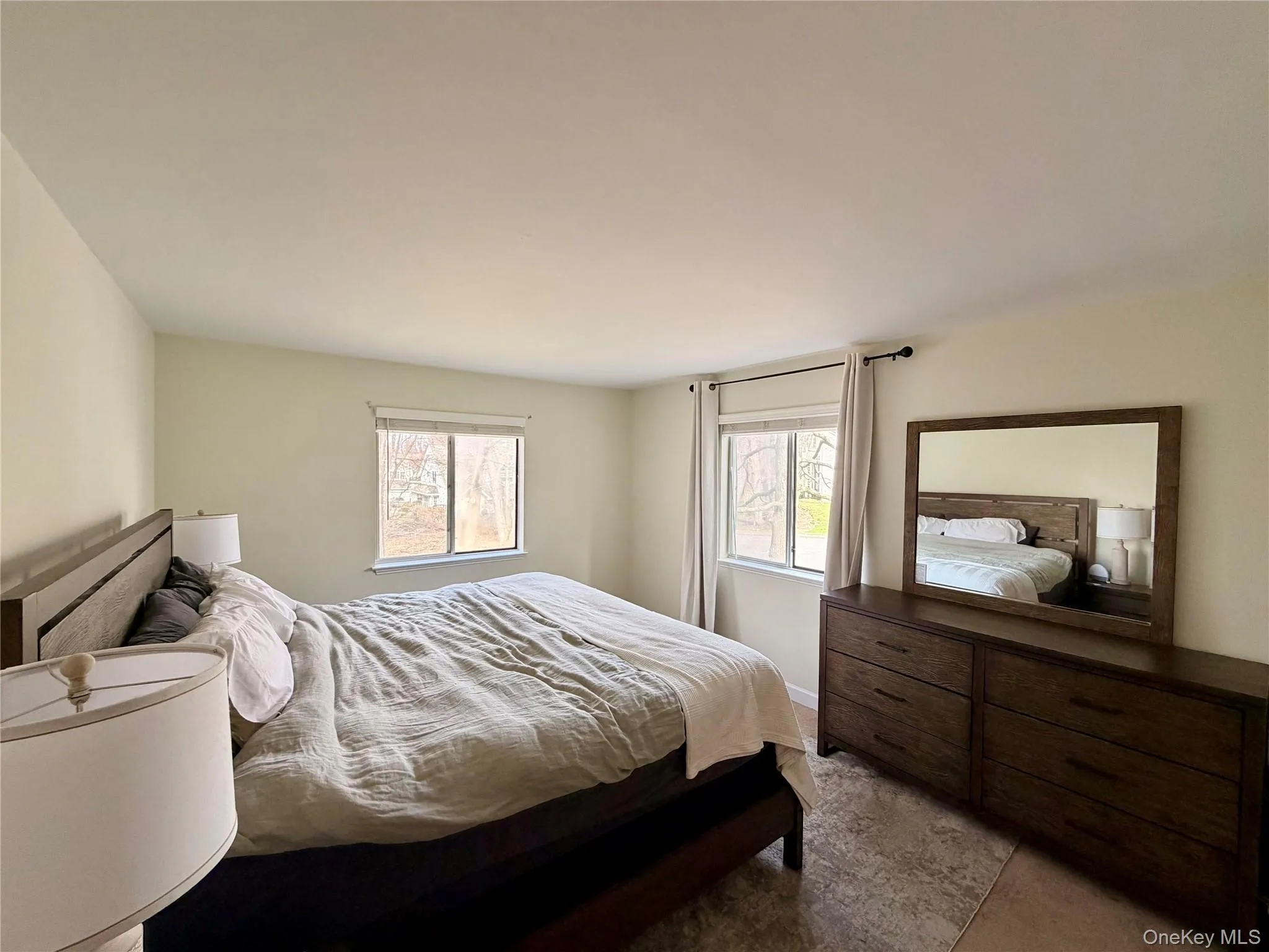 The primary bedroom is a serene retreat with dual windows framing wooded views, warm neutral tones, and plenty of room to unwind at the end of the day. The primary bedroom is a serene retreat with dual windows framing wooded views, warm neutral tones, and plenty of room to unwind at the end of the day.