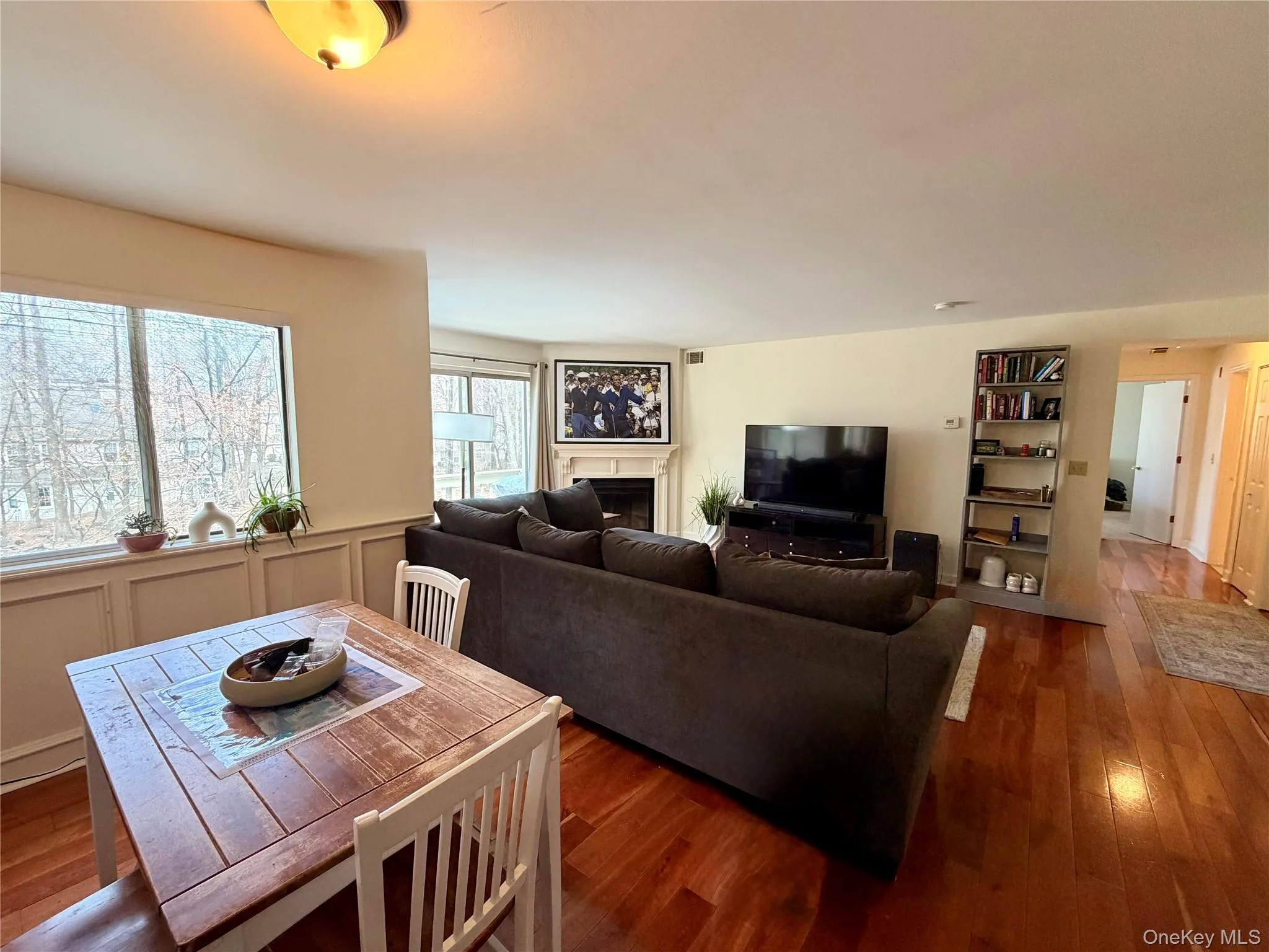 An open and airy flow connects the dining and living areas, with hardwood floors throughout, wooded views from oversized windows, and the wood-burning fireplace anchoring the space beautifully. An open and airy flow connects the dining and living areas, with hardwood floors throughout, wooded views from oversized windows, and the wood-burning fireplace anchoring the space beautifully.