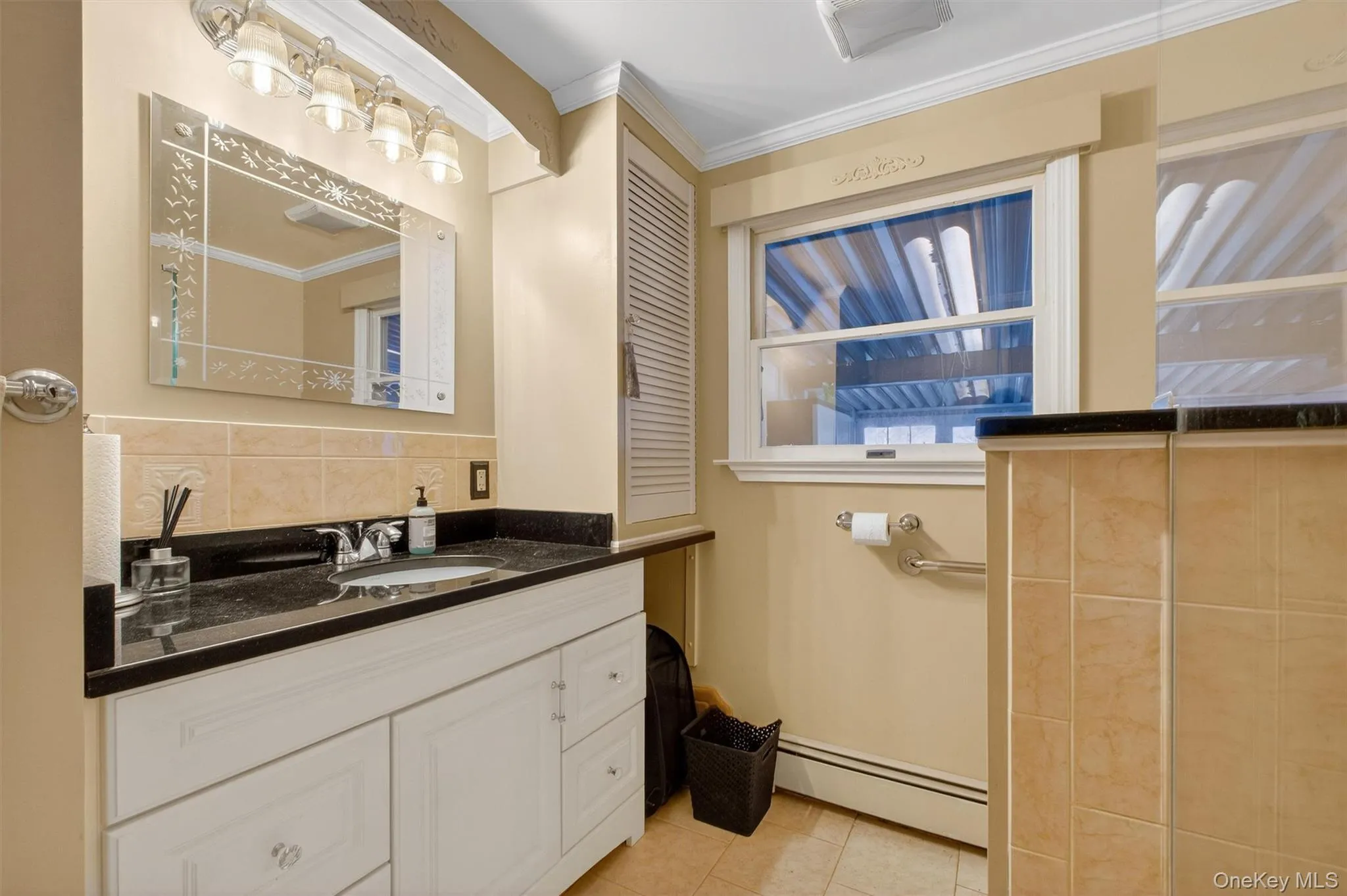 Bathroom with a baseboard radiator, vanity, light tile patterned floors, crown molding, and backsplash Bathroom with a baseboard radiator, vanity, light tile patterned floors, crown molding, and backsplash