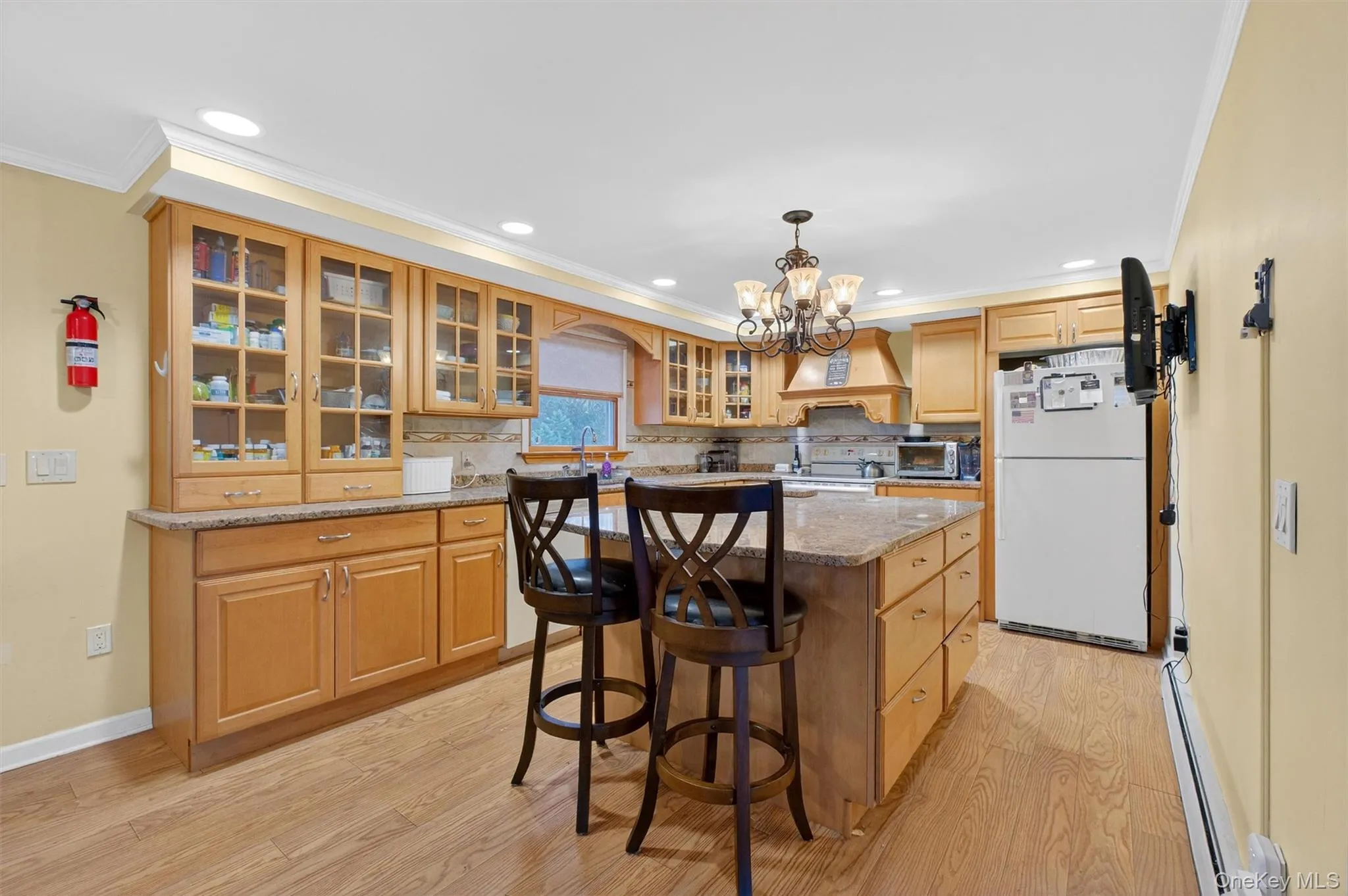 Kitchen featuring glass insert cabinets, white appliances, a kitchen island, light stone counters, and a chandelier Kitchen featuring glass insert cabinets, white appliances, a kitchen island, light stone counters, and a chandelier