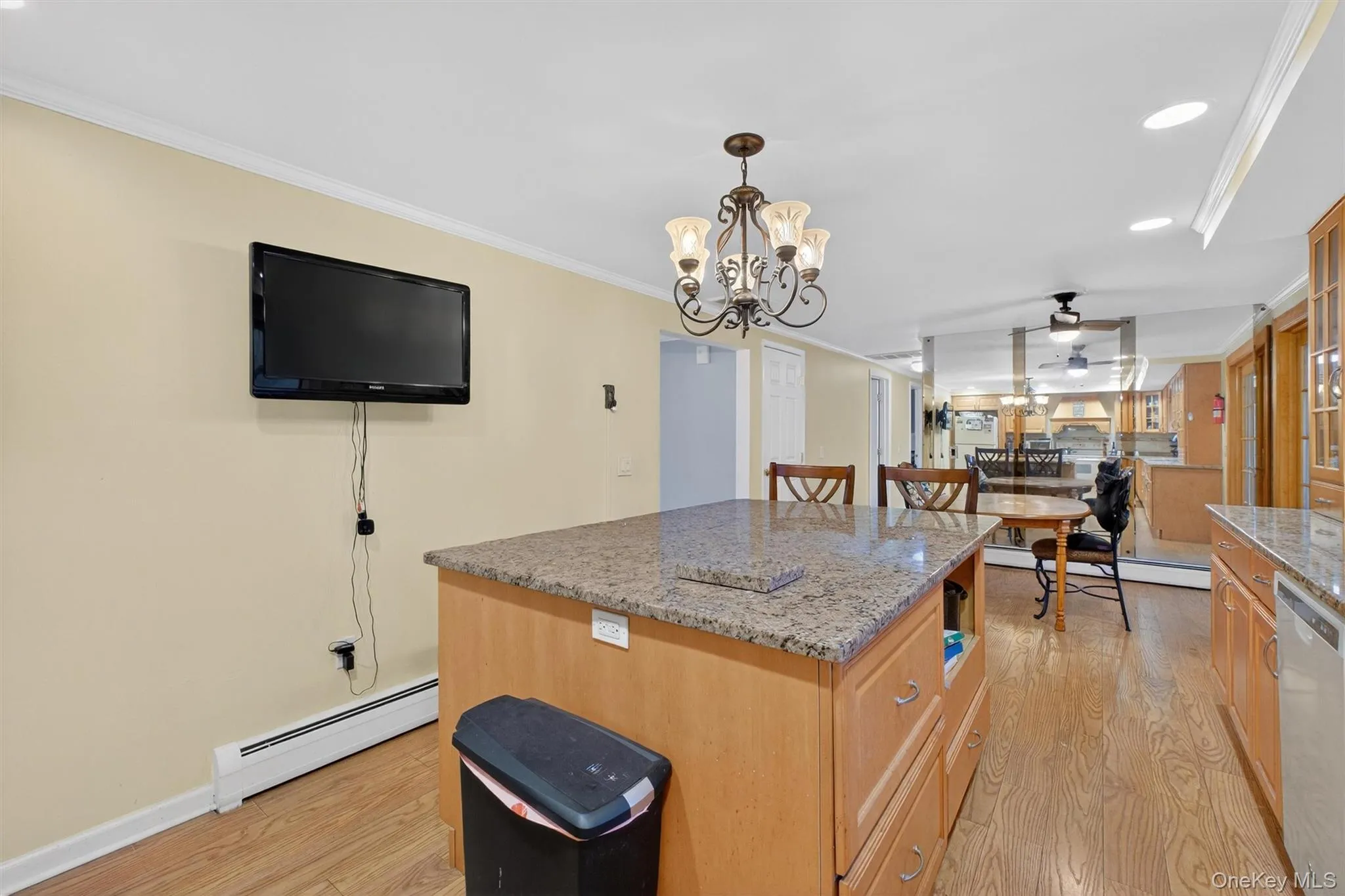 Kitchen featuring light stone countertops, ornamental molding, a ceiling fan, baseboard heating, and a center island Kitchen featuring light stone countertops, ornamental molding, a ceiling fan, baseboard heating, and a center island