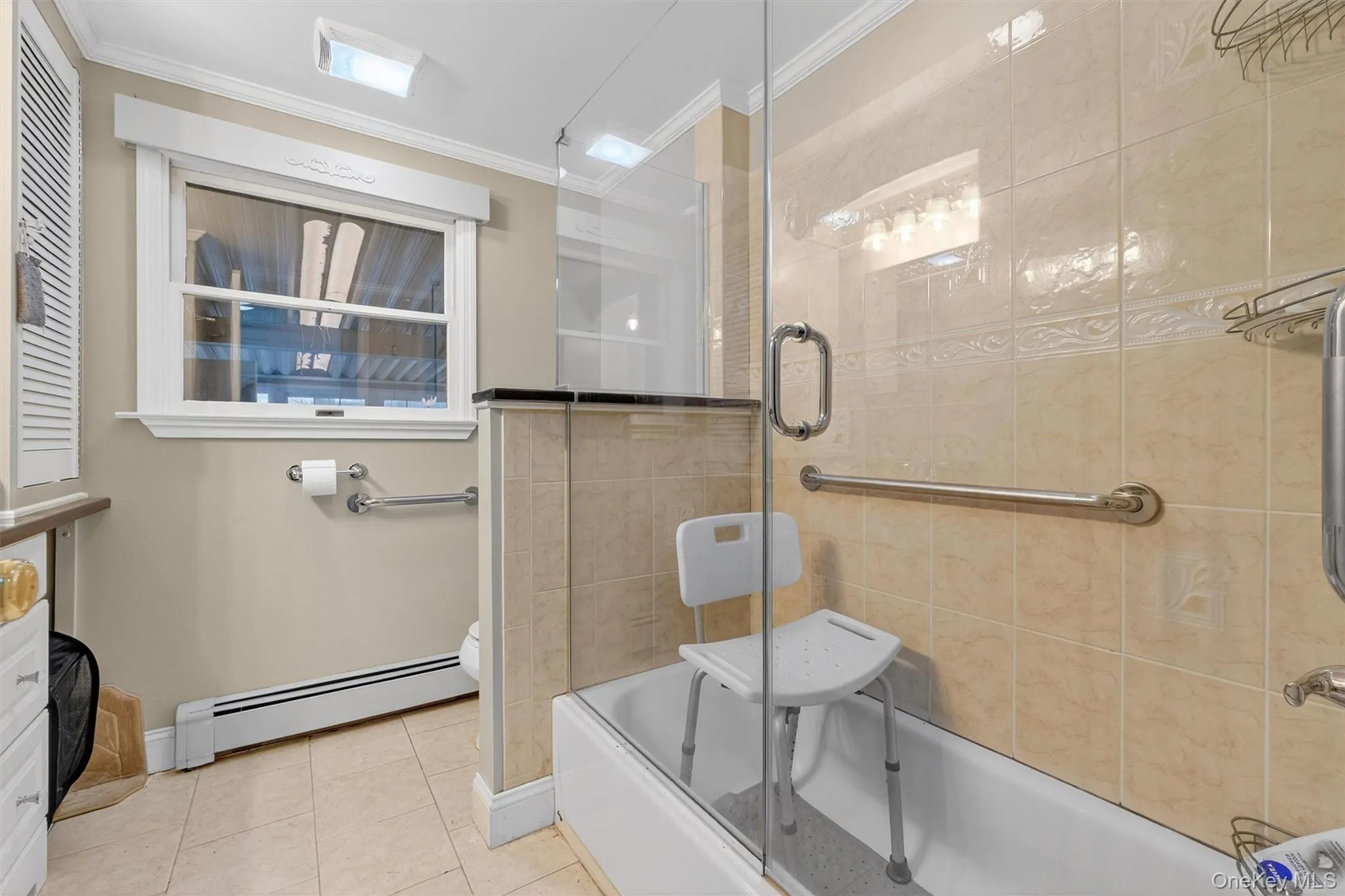Bathroom featuring ornamental molding, baseboard heating, combined bath / shower with glass door, and light tile patterned floors Bathroom featuring ornamental molding, baseboard heating, combined bath / shower with glass door, and light tile patterned floors