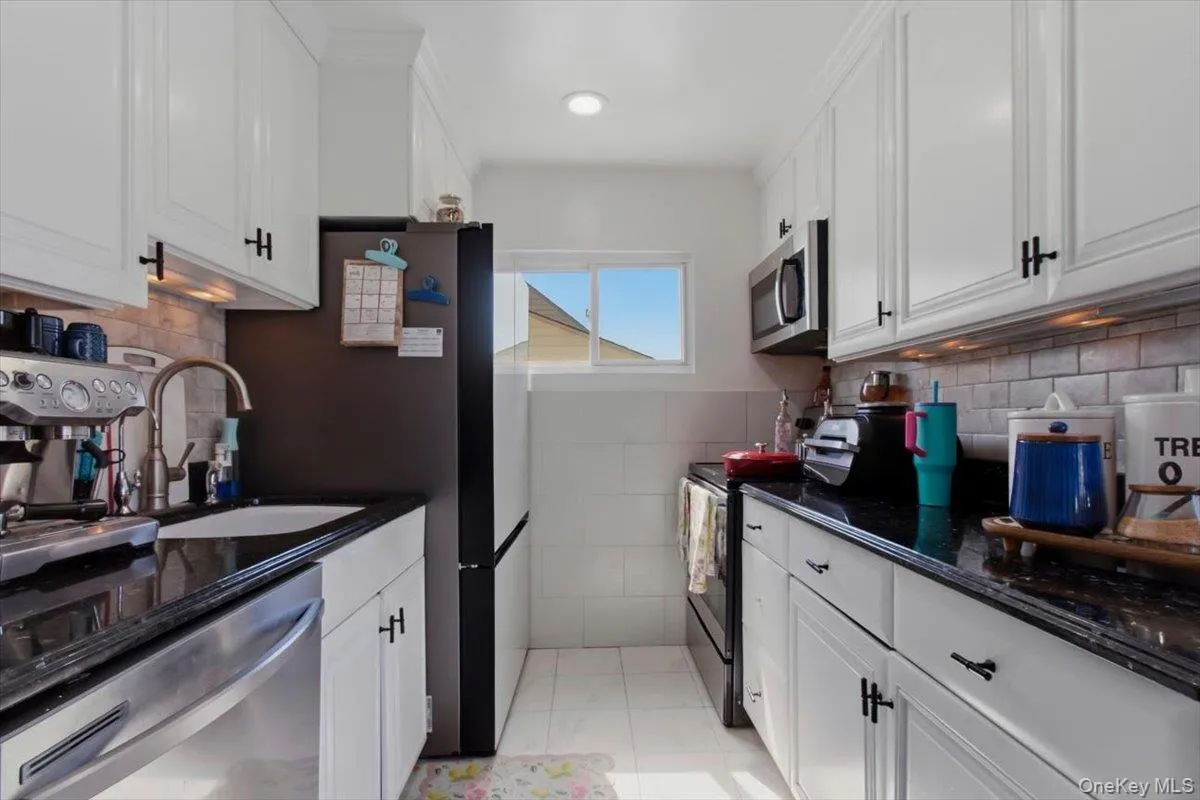 Kitchen with white cabinetry, stainless steel appliances, dark stone counters, light tile patterned floors, and recessed lighting Kitchen with white cabinetry, stainless steel appliances, dark stone counters, light tile patterned floors, and recessed lighting