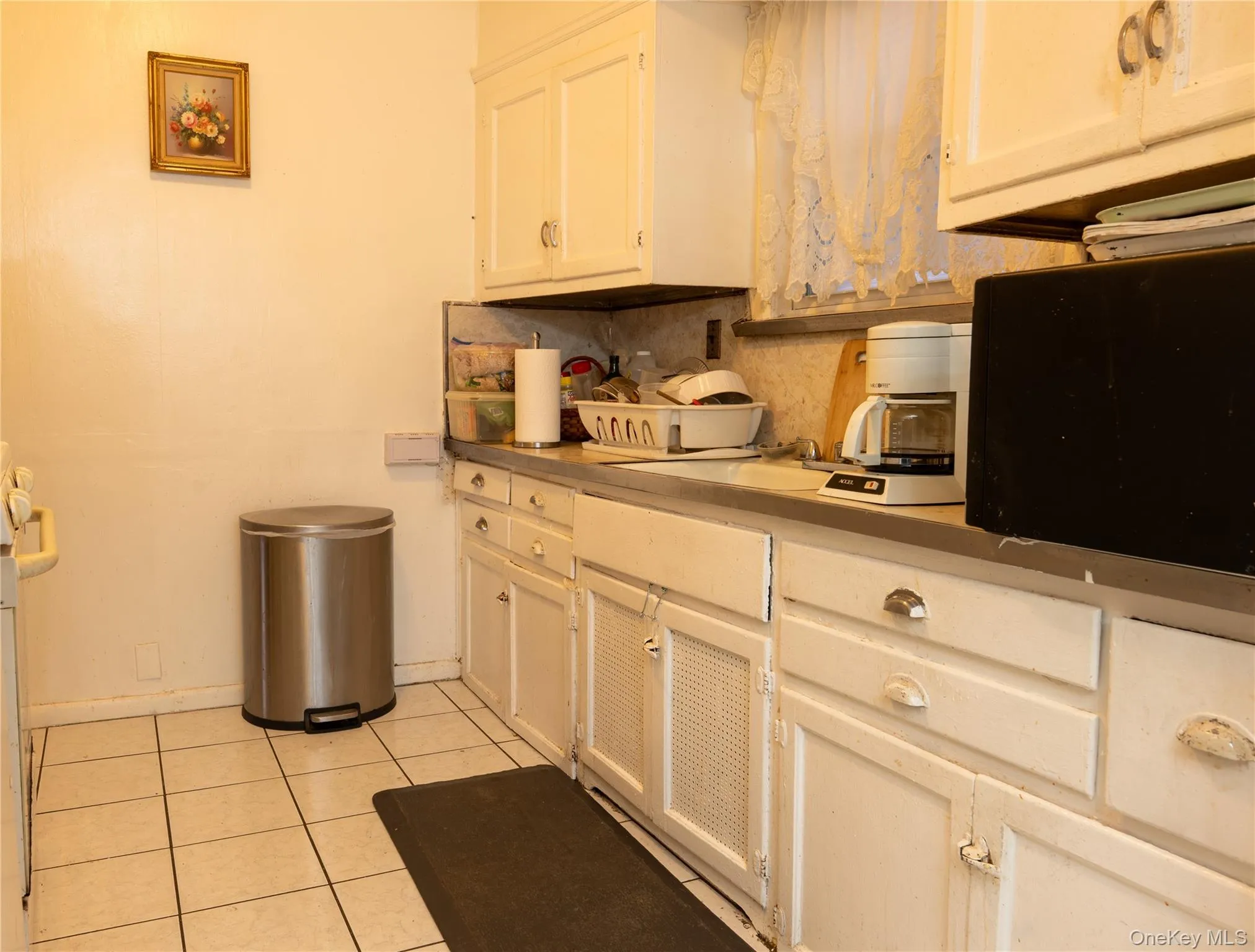 Kitchen featuring white cabinetry, light tile patterned flooring, black microwave, and countertops Kitchen featuring white cabinetry, light tile patterned flooring, black microwave, and countertops
