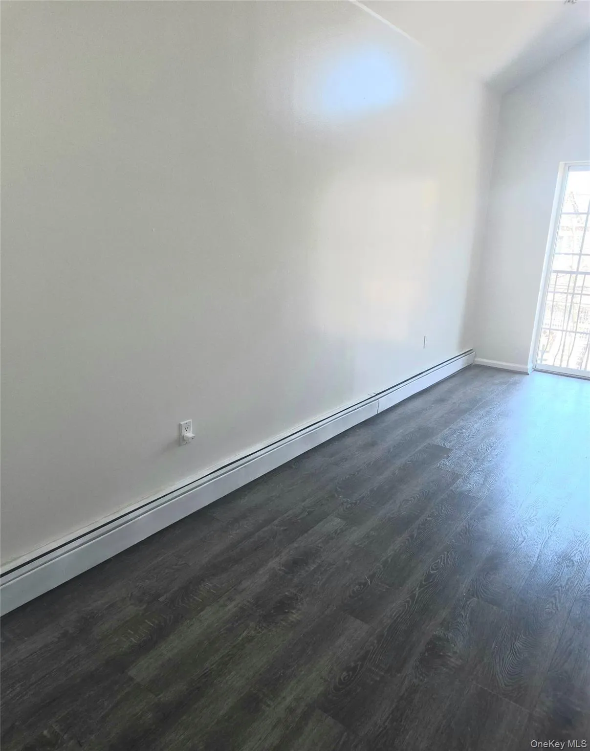Empty room with a baseboard radiator, dark wood-type flooring, and vaulted ceiling Empty room with a baseboard radiator, dark wood-type flooring, and vaulted ceiling