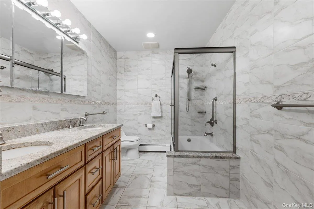 Renovated and tiled, hall bathroom with granite double sink vanity, triple mirrored medicine chests, & a large glass enclosed tub/shower. Renovated and tiled, hall bathroom with granite double sink vanity, triple mirrored medicine chests, & a large glass enclosed tub/shower.