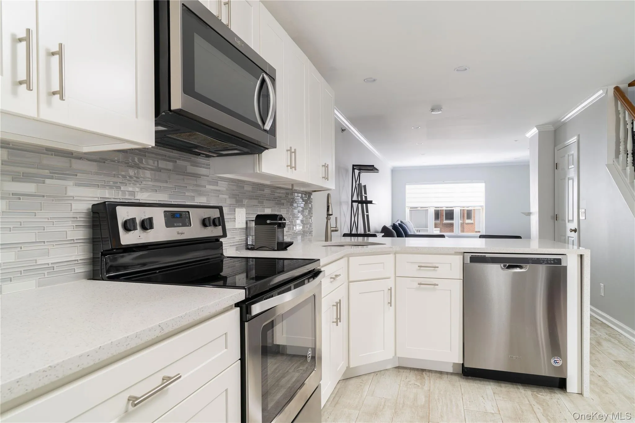Kitchen featuring stainless steel appliances, white cabinets, a peninsula, decorative backsplash, and crown molding Kitchen featuring stainless steel appliances, white cabinets, a peninsula, decorative backsplash, and crown molding
