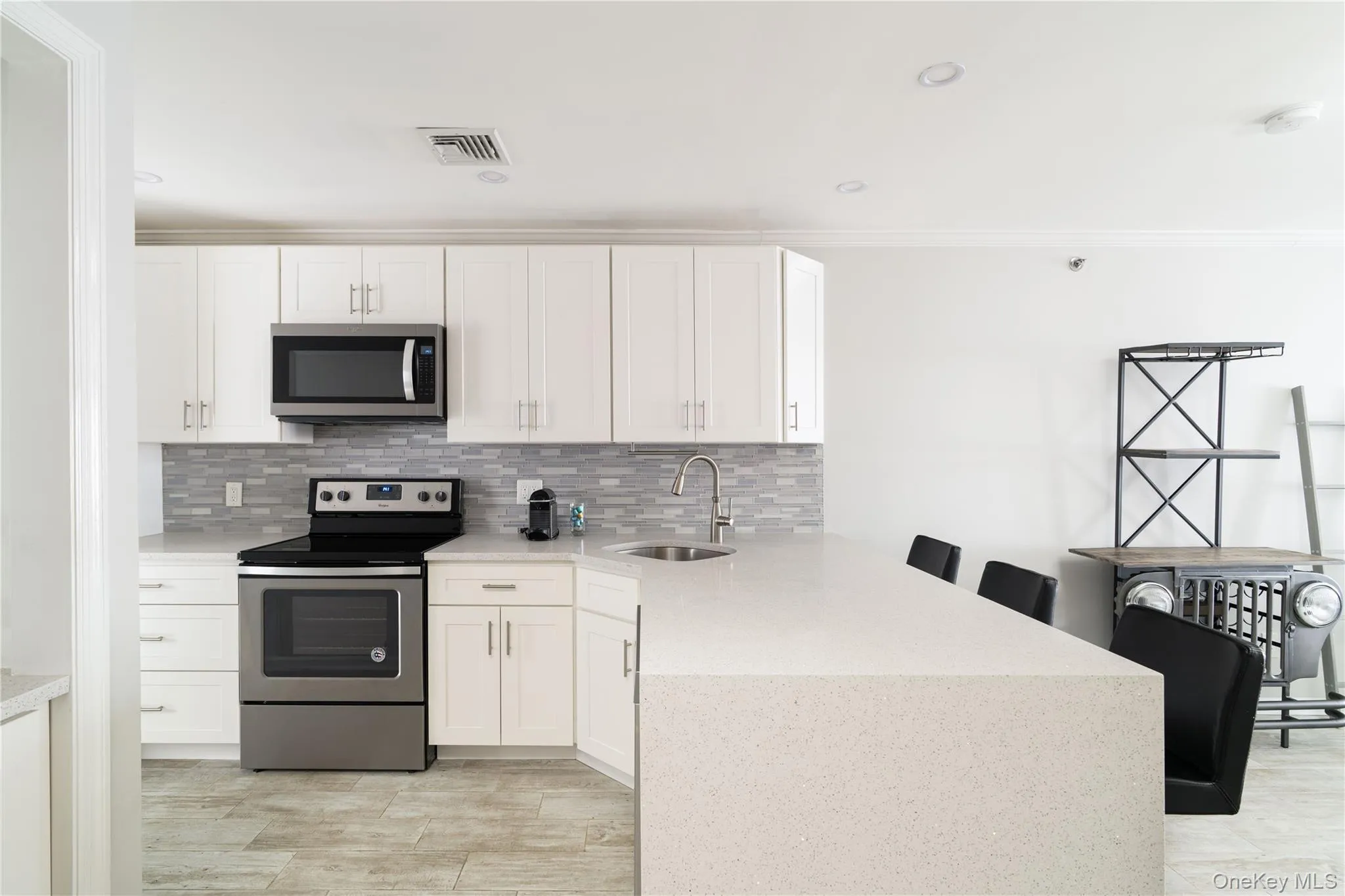 Kitchen featuring stainless steel appliances, a peninsula, white cabinetry, backsplash, and ornamental molding Kitchen featuring stainless steel appliances, a peninsula, white cabinetry, backsplash, and ornamental molding
