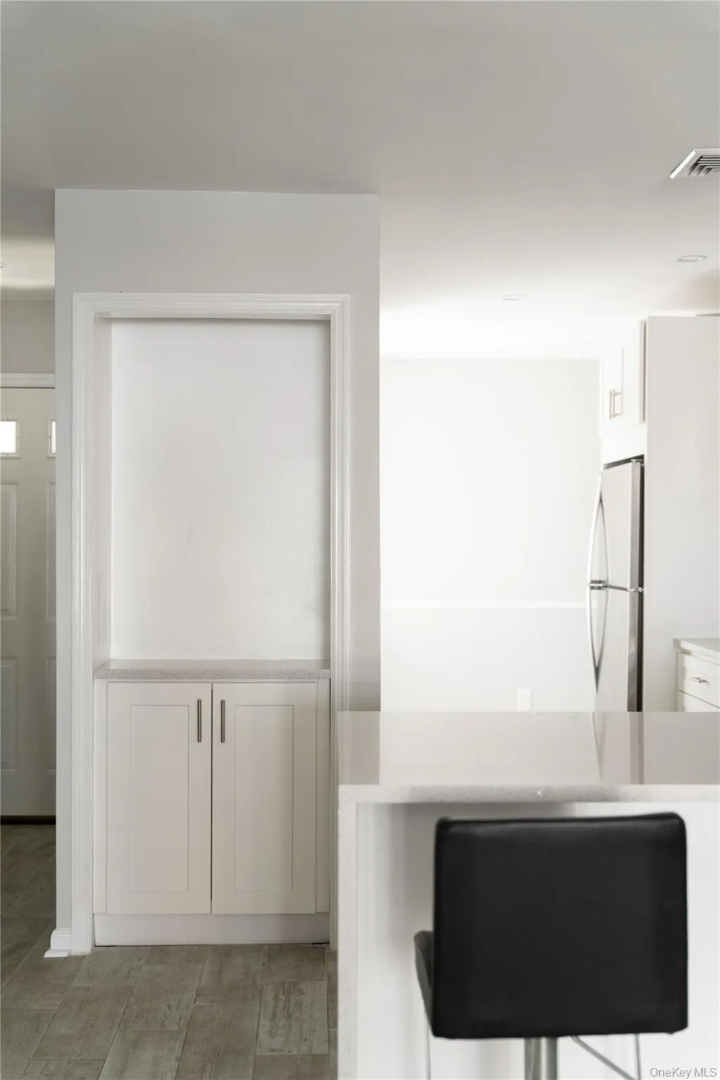 Detailed view of light countertops, freestanding refrigerator, white cabinetry, and light wood-style floors Detailed view of light countertops, freestanding refrigerator, white cabinetry, and light wood-style floors
