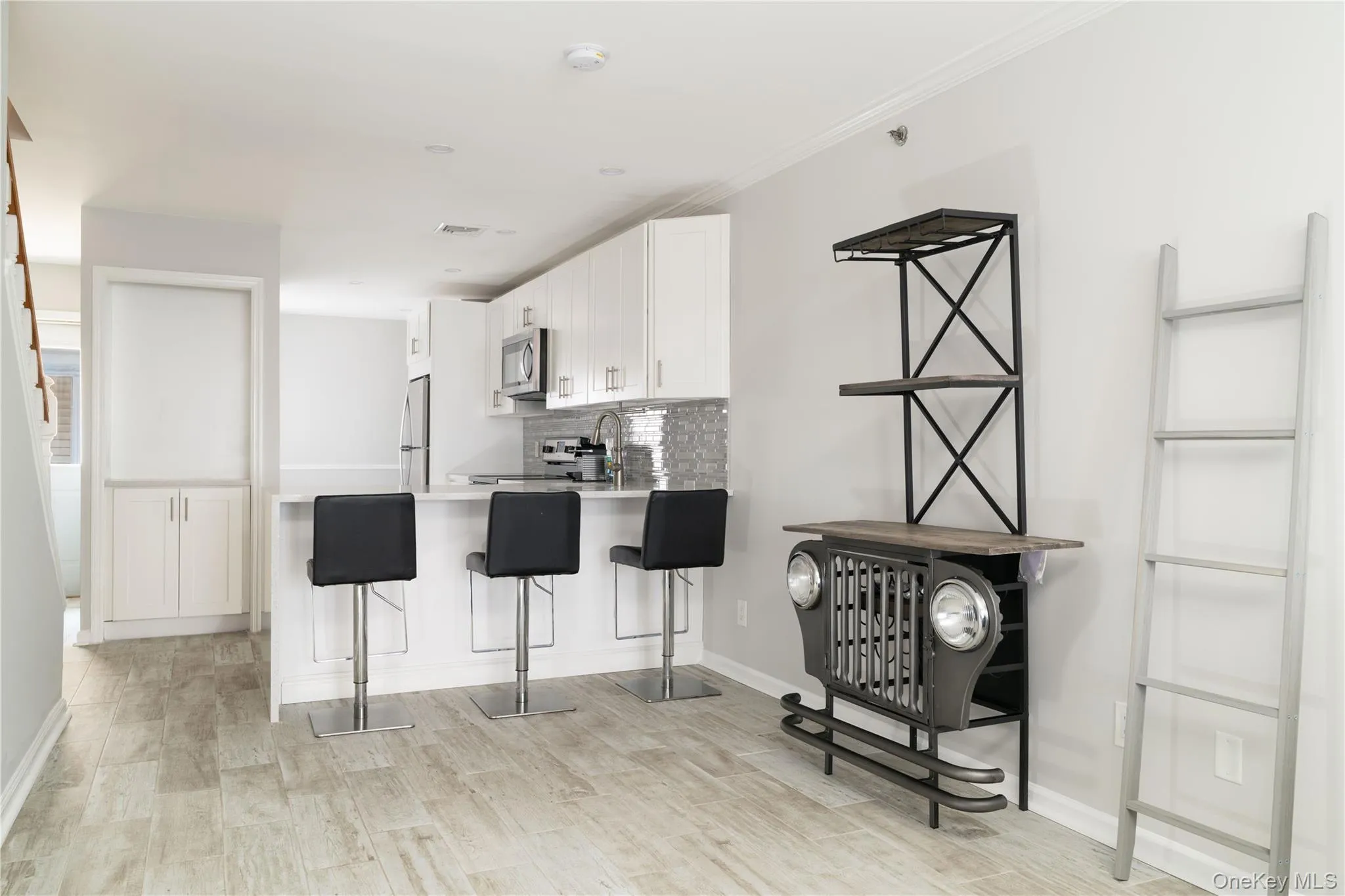 Kitchen featuring light wood-style flooring, decorative backsplash, white cabinets, a kitchen bar, and light countertops Kitchen featuring light wood-style flooring, decorative backsplash, white cabinets, a kitchen bar, and light countertops
