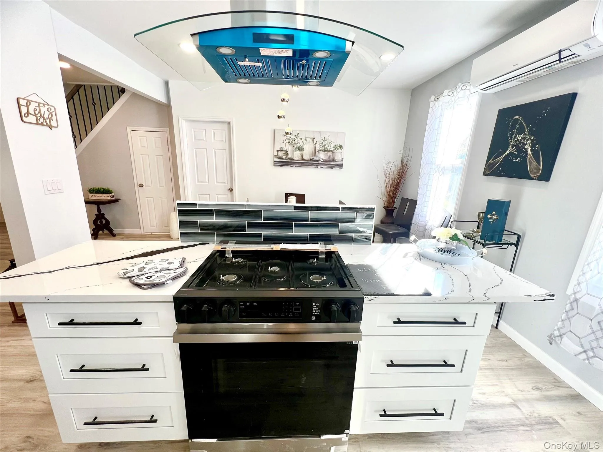 Kitchen with ventilation hood, black gas stove, light wood-style floors, light stone counters, and an AC wall unit Kitchen with ventilation hood, black gas stove, light wood-style floors, light stone counters, and an AC wall unit