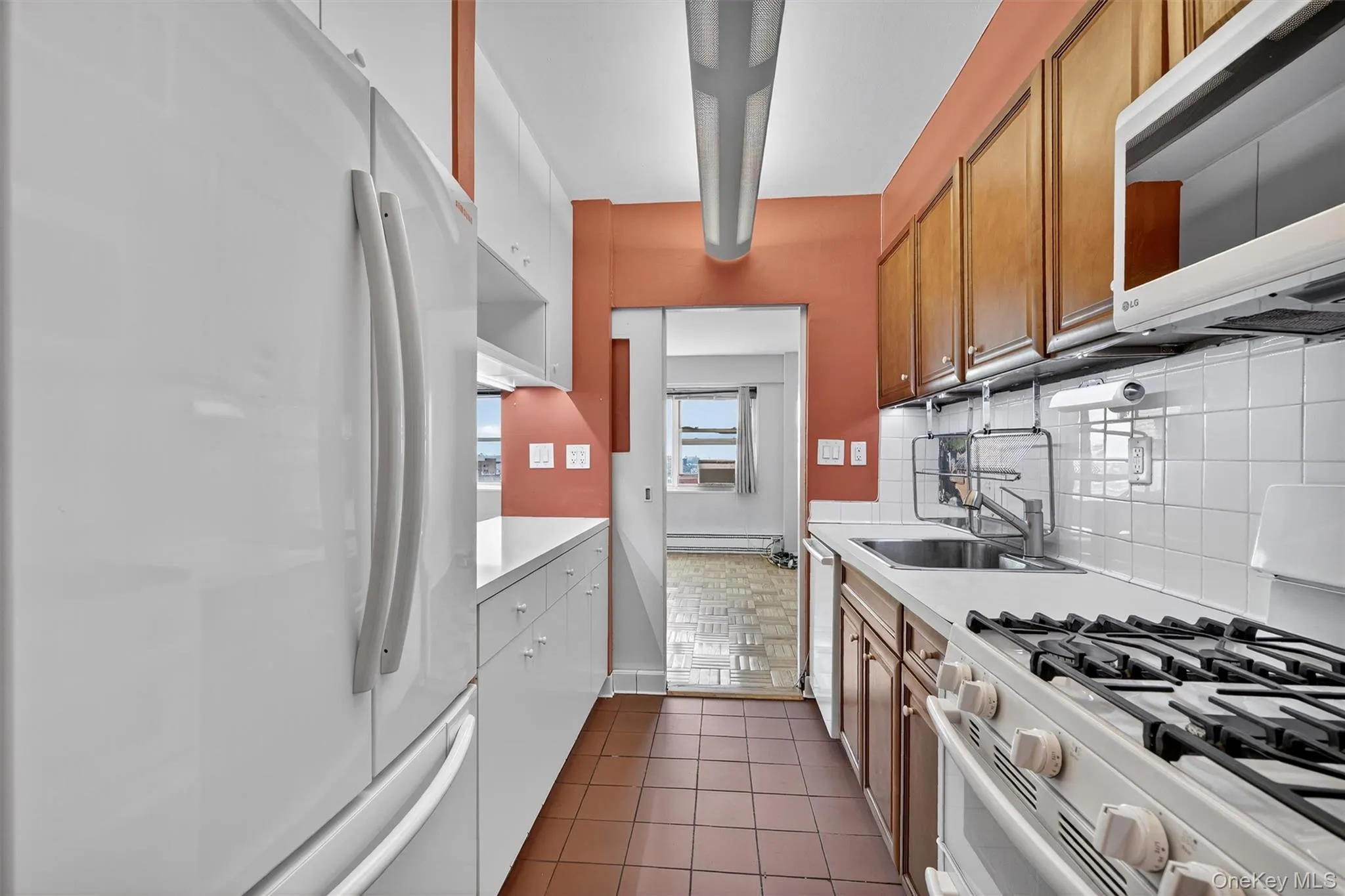 Kitchen featuring white appliances, light countertops, decorative backsplash, brown cabinetry, and a baseboard radiator Kitchen featuring white appliances, light countertops, decorative backsplash, brown cabinetry, and a baseboard radiator