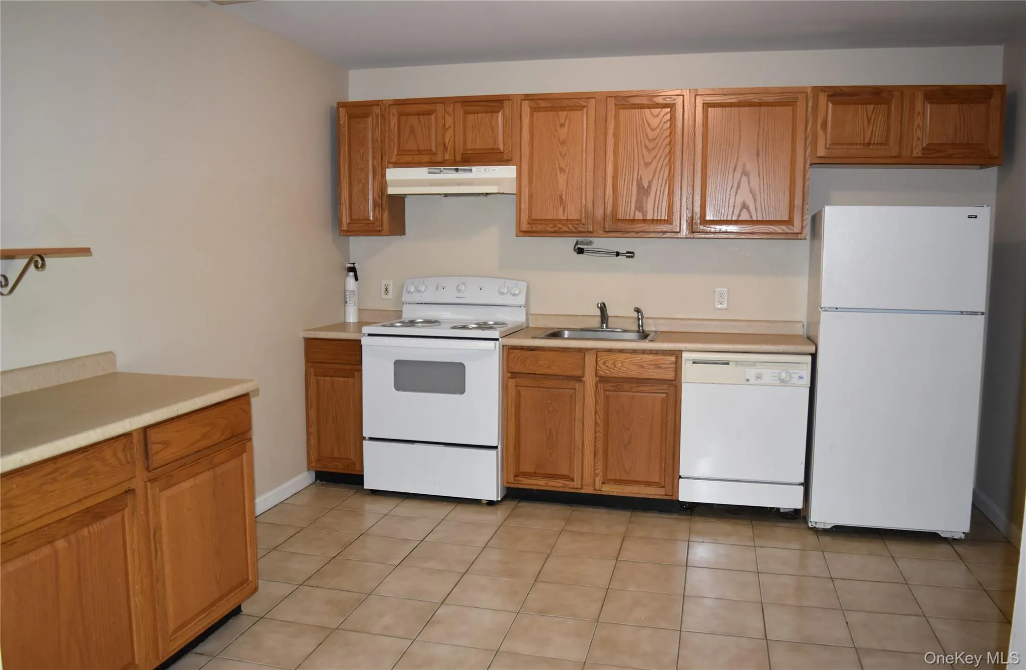 Kitchen with white appliances, under cabinet range hood, a sink, light countertops, and brown cabinetry Kitchen with white appliances, under cabinet range hood, a sink, light countertops, and brown cabinetry
