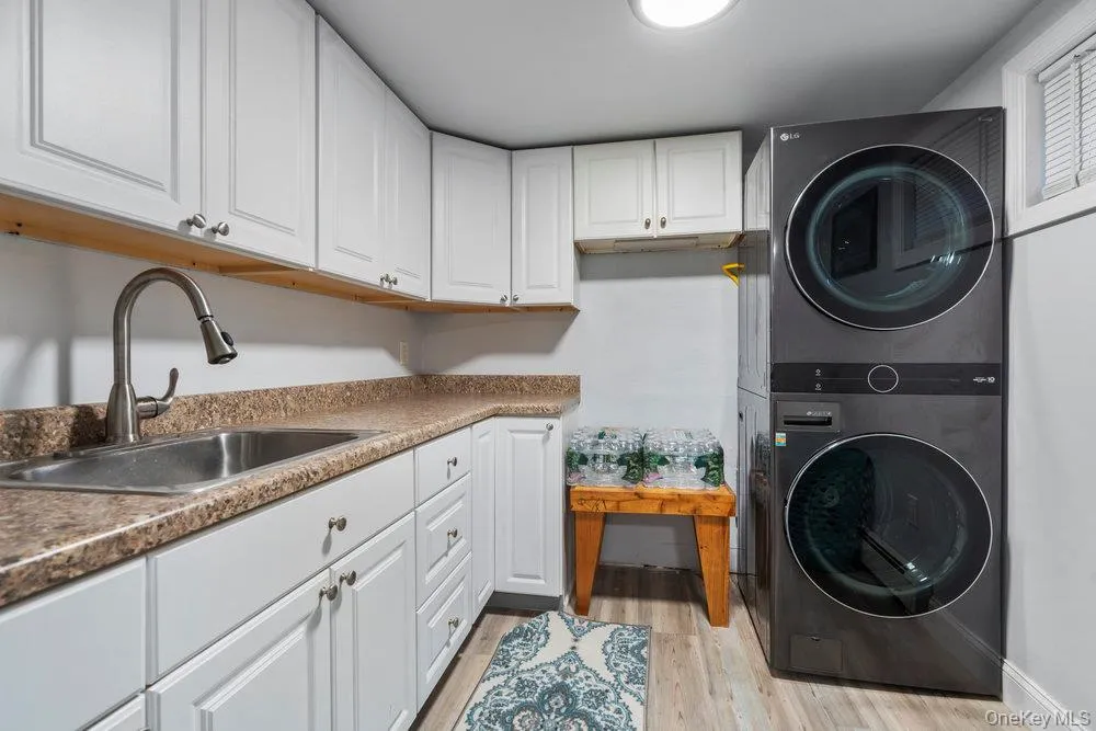 Laundry area featuring stacked washer and clothes dryer, light wood finished floors, and cabinet space Laundry area featuring stacked washer and clothes dryer, light wood finished floors, and cabinet space