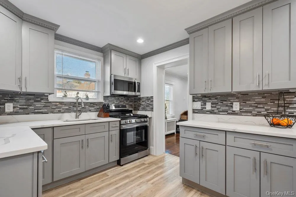 Kitchen featuring gray cabinetry, stainless steel appliances, light wood finished floors, light stone countertops, and ornamental molding Kitchen featuring gray cabinetry, stainless steel appliances, light wood finished floors, light stone countertops, and ornamental molding