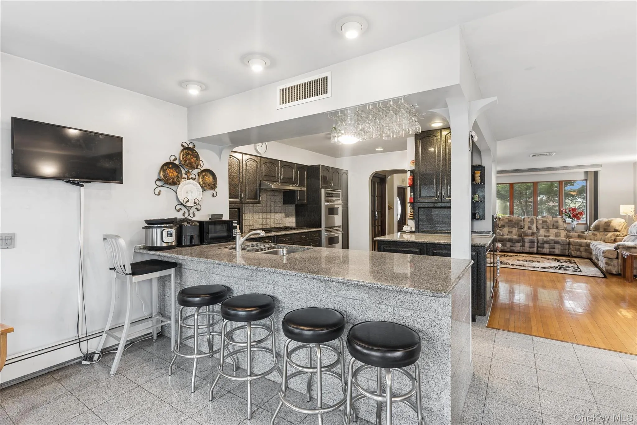 Kitchen featuring a kitchen bar, arched walkways, a peninsula, a baseboard radiator, and light stone counters Kitchen featuring a kitchen bar, arched walkways, a peninsula, a baseboard radiator, and light stone counters