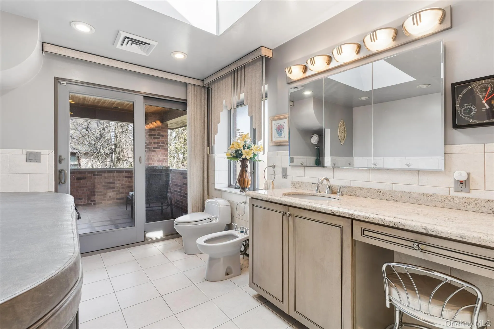 Master Bathroom Suite with a bidet, vanity, tile walls, a skylight, and light tile patterned floors Master Bathroom Suite with a bidet, vanity, tile walls, a skylight, and light tile patterned floors