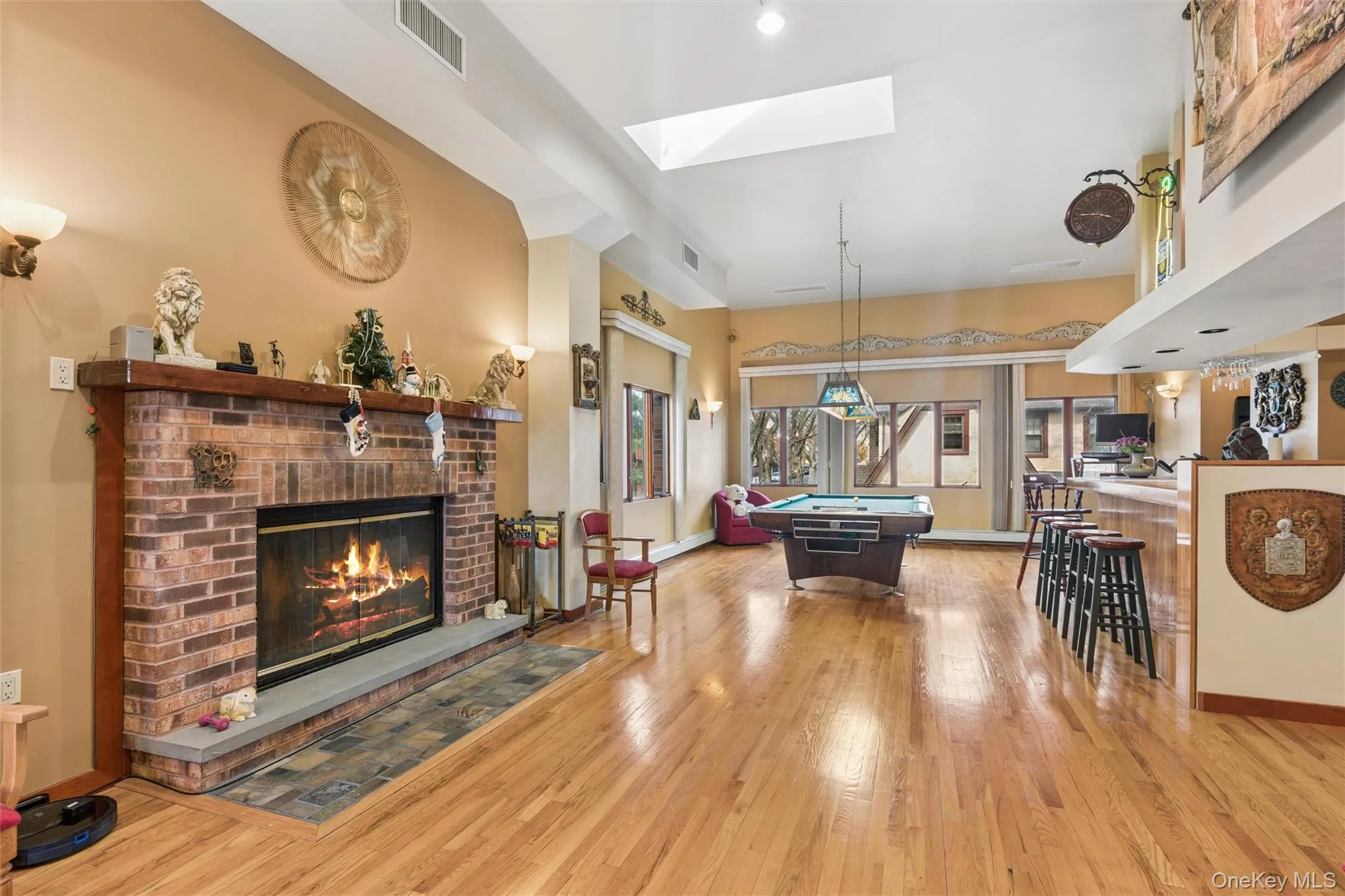 Playroom with a skylight, a fireplace, light wood-style flooring, billiards, and a high ceiling Playroom with a skylight, a fireplace, light wood-style flooring, billiards, and a high ceiling