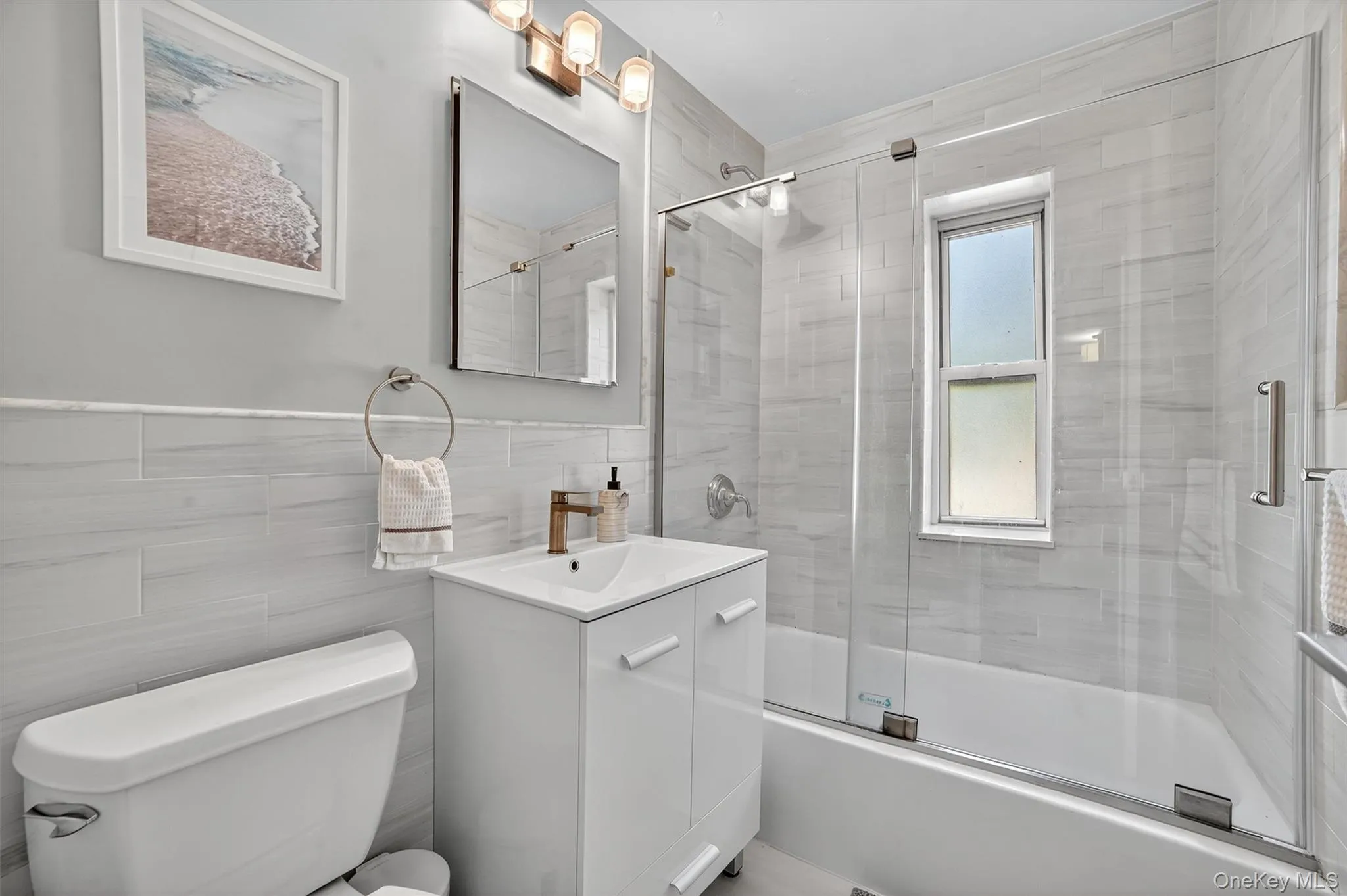 Bathroom featuring vanity, bath / shower combo with glass door, tile walls and window. Bathroom featuring vanity, bath / shower combo with glass door, tile walls and window.