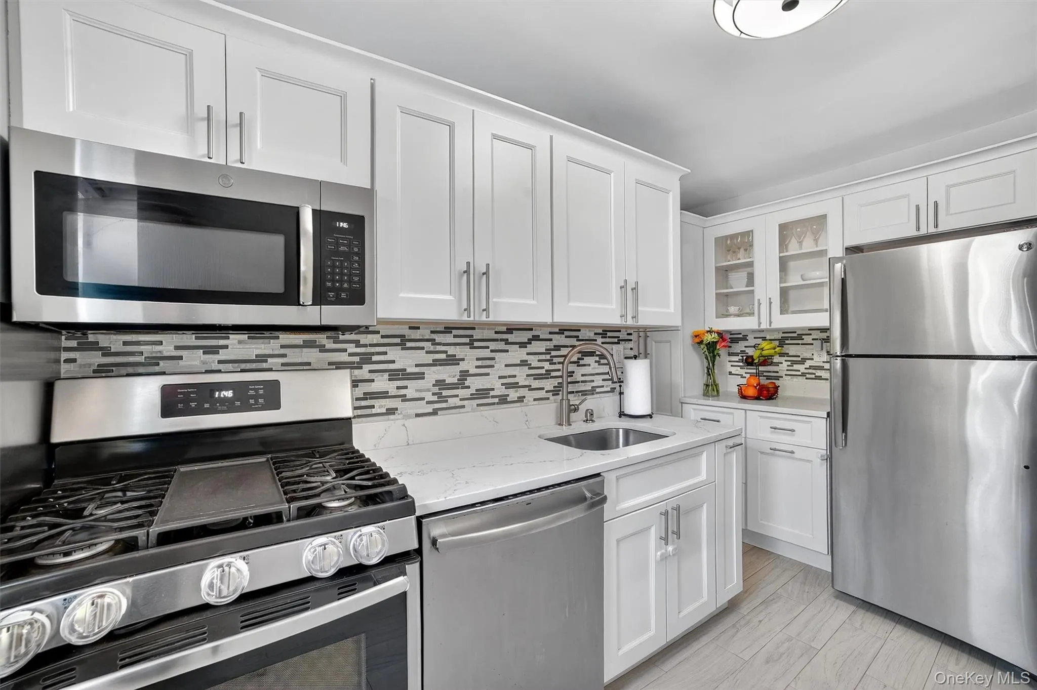 Kitchen featuring stainless steel appliances, decorative backsplash, white cabinetry, and light quartz countertops Kitchen featuring stainless steel appliances, decorative backsplash, white cabinetry, and light quartz countertops
