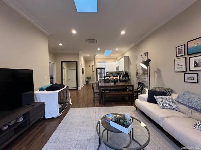 Living room featuring a skylight, recessed lighting, dark wood-style flooring, and ornamental molding Living room featuring a skylight, recessed lighting, dark wood-style flooring, and ornamental molding