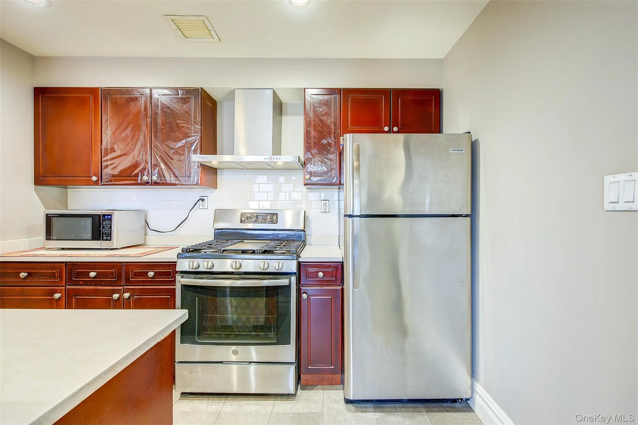 Kitchen featuring bold wood finish cabinetry, stainless steel appliances, light countertops, and decorative backsplash Kitchen featuring bold wood finish cabinetry, stainless steel appliances, light countertops, and decorative backsplash