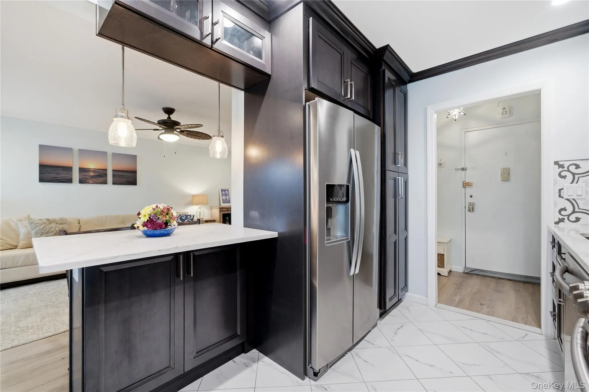 Kitchen featuring stainless steel fridge, open floor plan, light stone counters, light marble finish floors, and crown molding Kitchen featuring stainless steel fridge, open floor plan, light stone counters, light marble finish floors, and crown molding