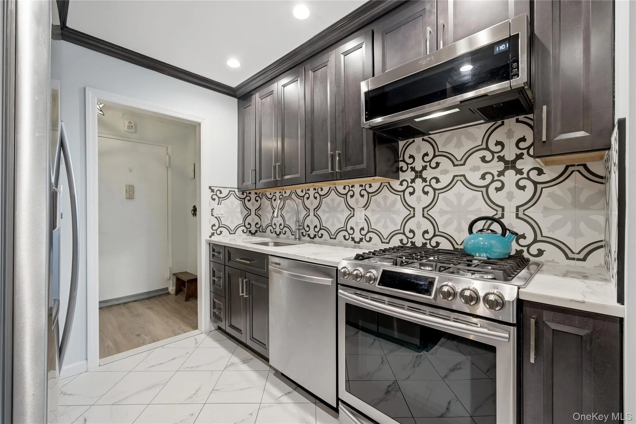 Kitchen featuring stainless steel appliances, light marble finish flooring, light stone countertops, dark wood finish cabinets, and ornamental molding Kitchen featuring stainless steel appliances, light marble finish flooring, light stone countertops, dark wood finish cabinets, and ornamental molding