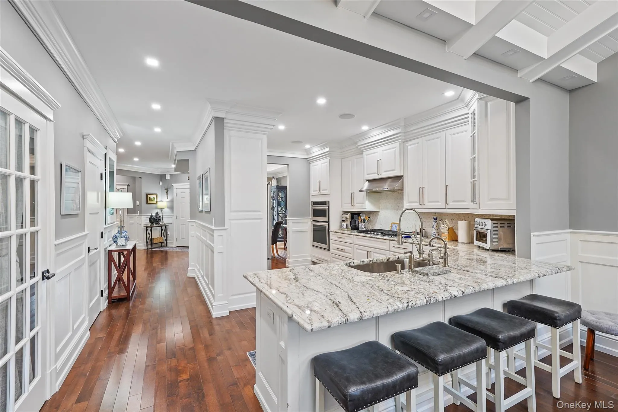 Kitchen with a decorative wall, light stone counters, a kitchen bar, white cabinets, and dark wood-type flooring Kitchen with a decorative wall, light stone counters, a kitchen bar, white cabinets, and dark wood-type flooring